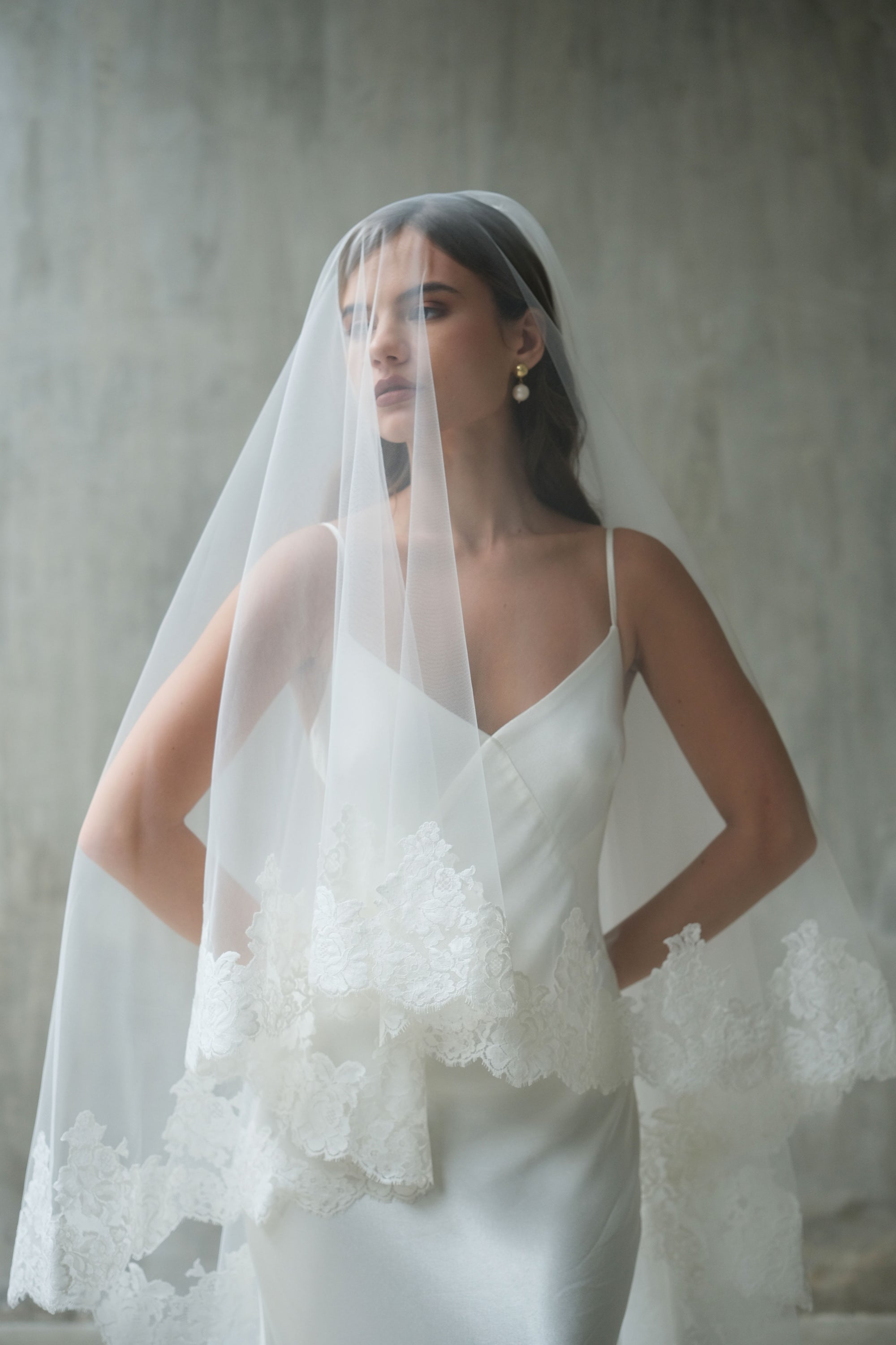 Half length front facing bride wears two tier romantic lace trimmed veil shown with blusher down