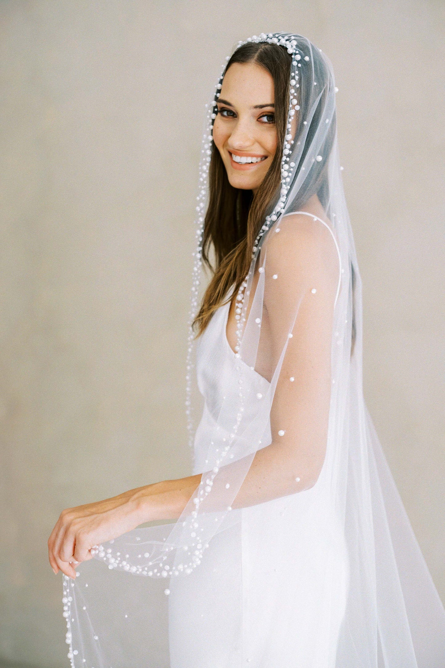 Bride models long mantilla veil edged pearls in varying sizes and featuring a pearl scatter overall