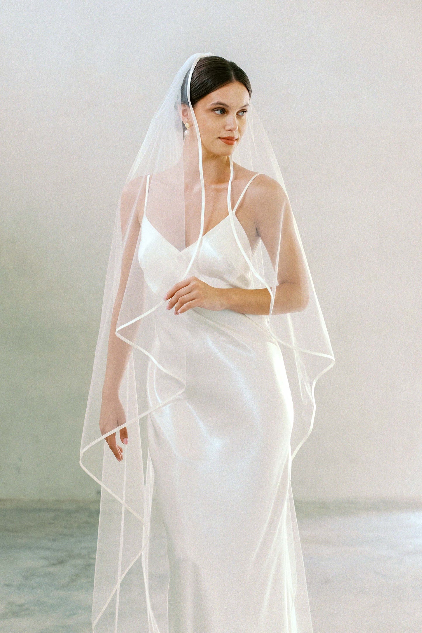Frontal half length shot of model wearing long, one tier bridal veil edged with satin ribbon