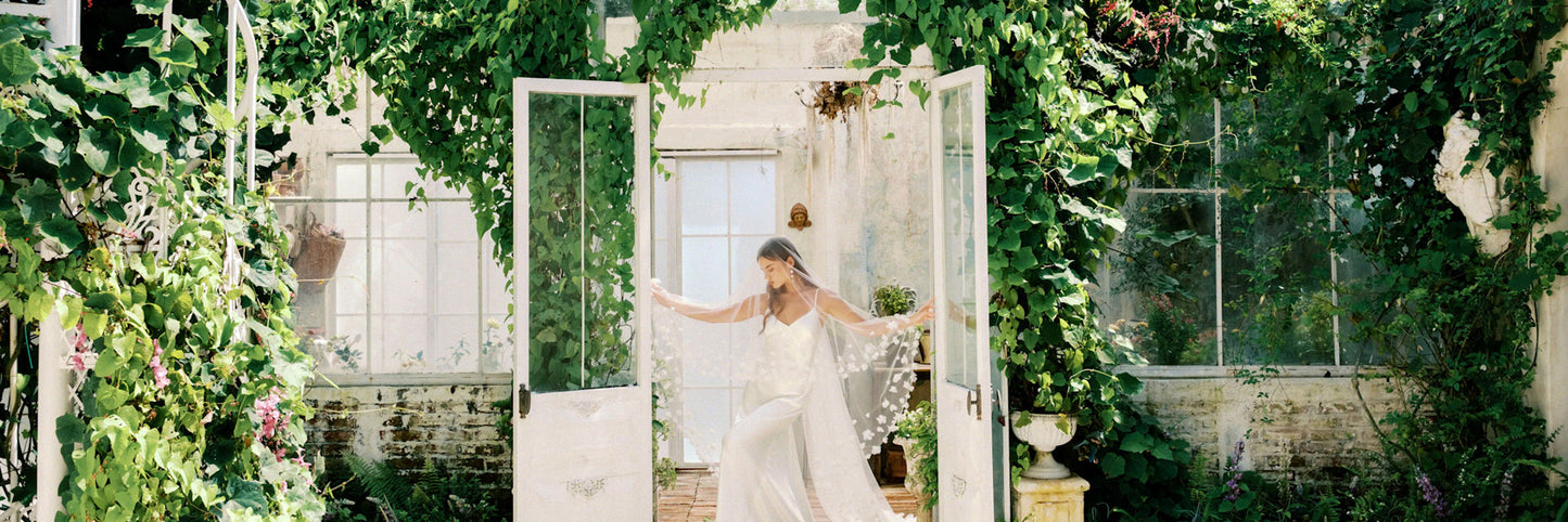 Bride in romantic greenhouse setting holds out veil embellished with fabric flowers