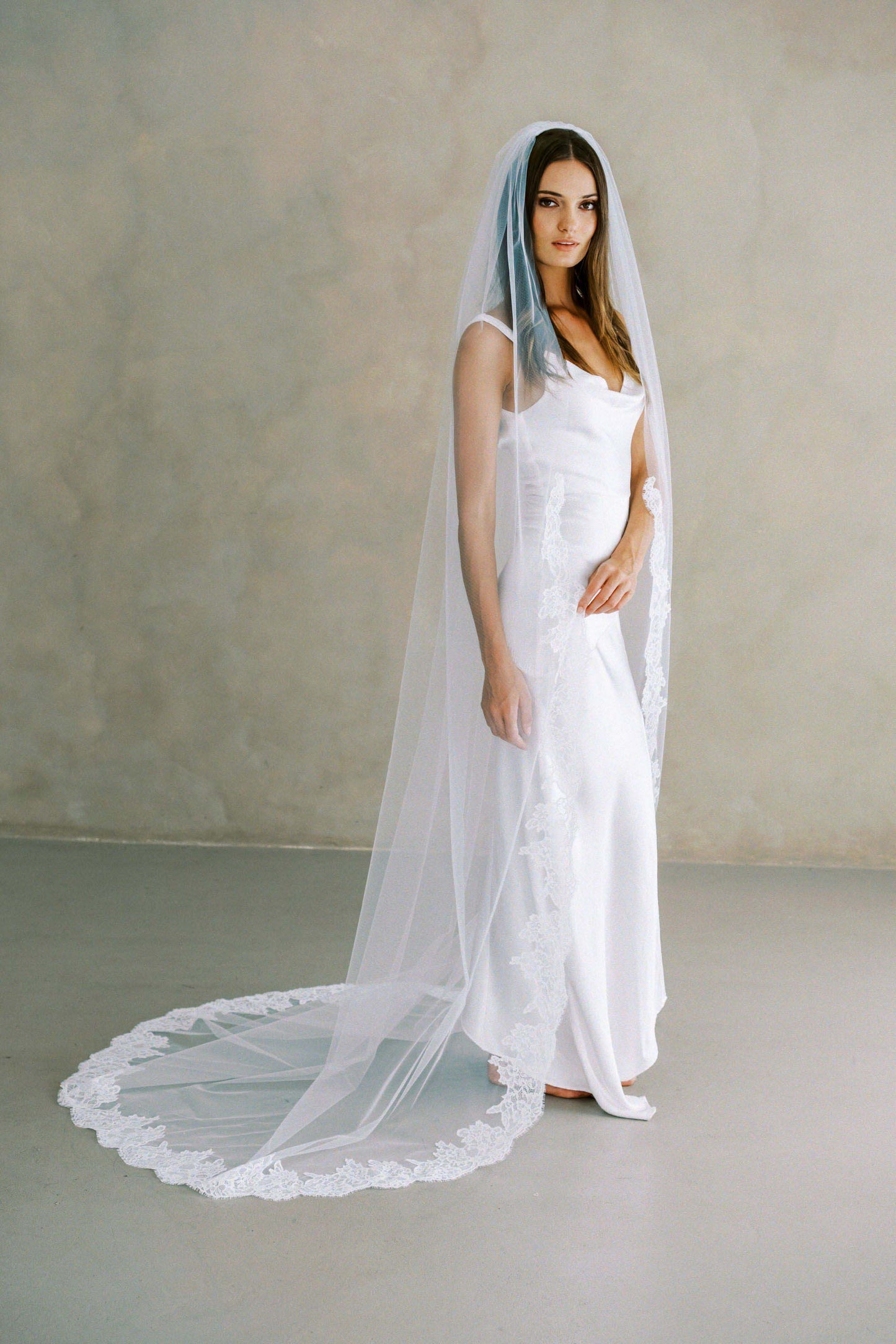 Model wears a lace wedding veil, one tier veil with partial lace trim.