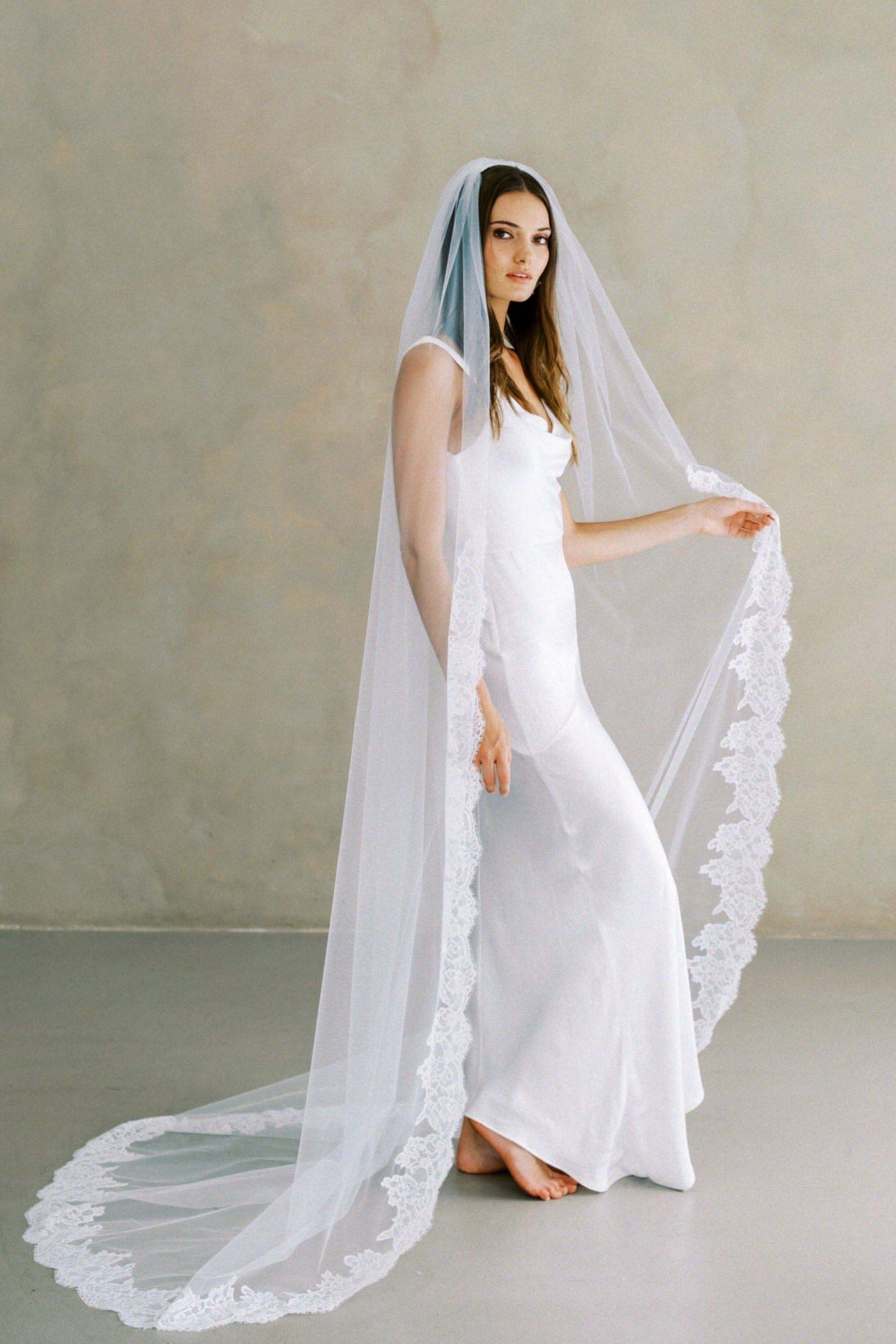 Model wears a lace wedding veil, one tier veil with partial lace trim.