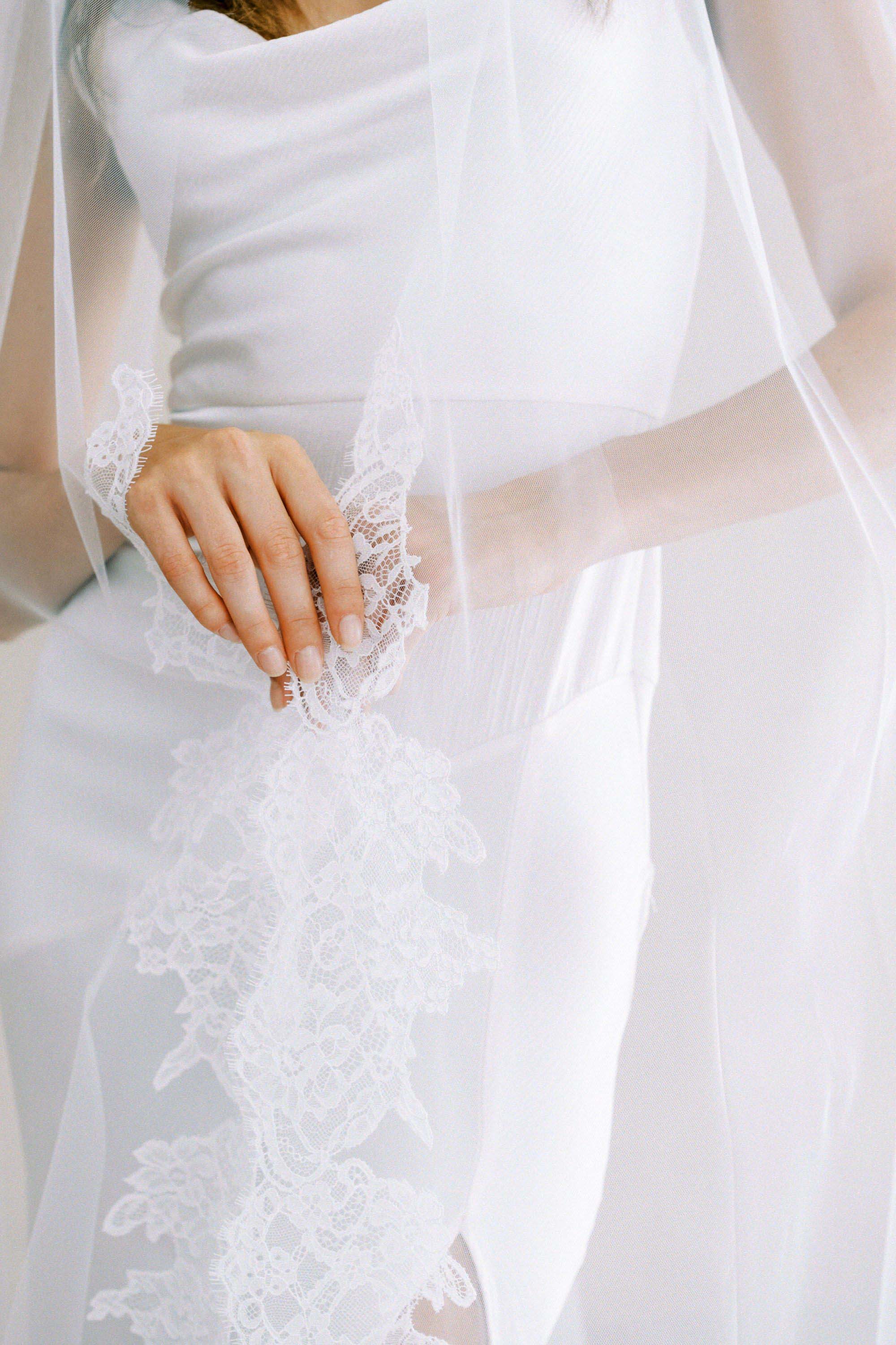 Model wears a lace wedding veil, one tier veil with partial lace trim.
