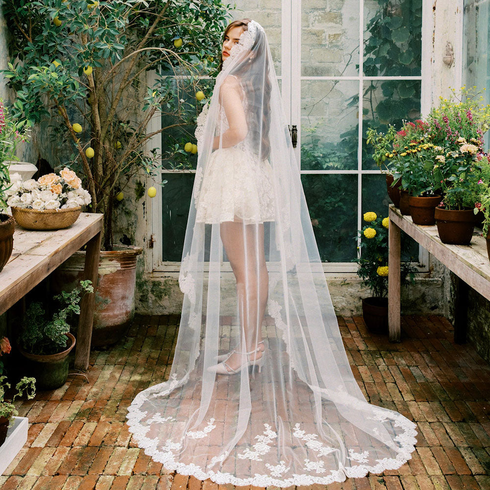 Bride models long mantilla veil trimmed with lace and featuring lace applique in rustic garden setting