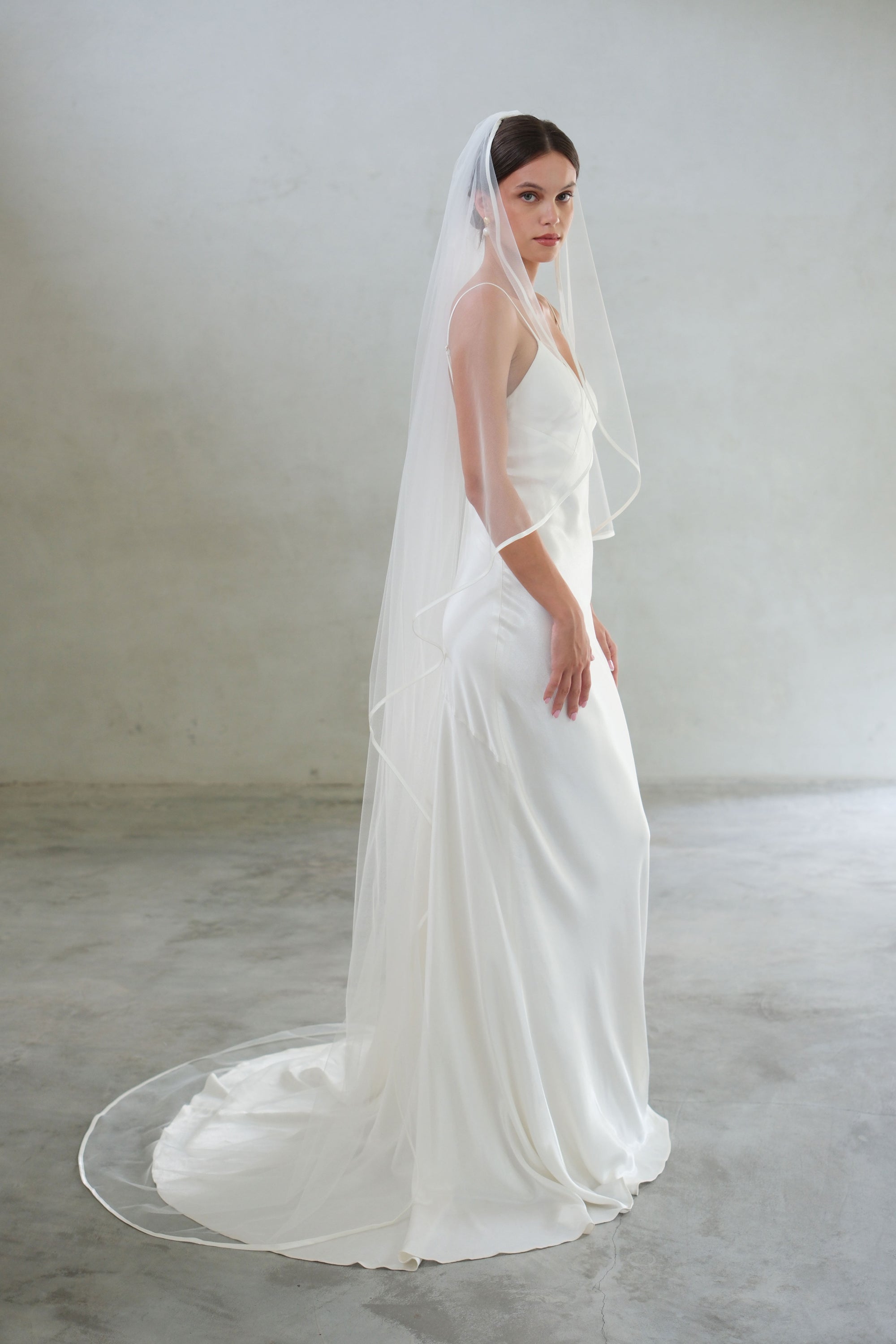 Full length side view of bride wearing long, one-tier veil trimmed with fine satin ribbon