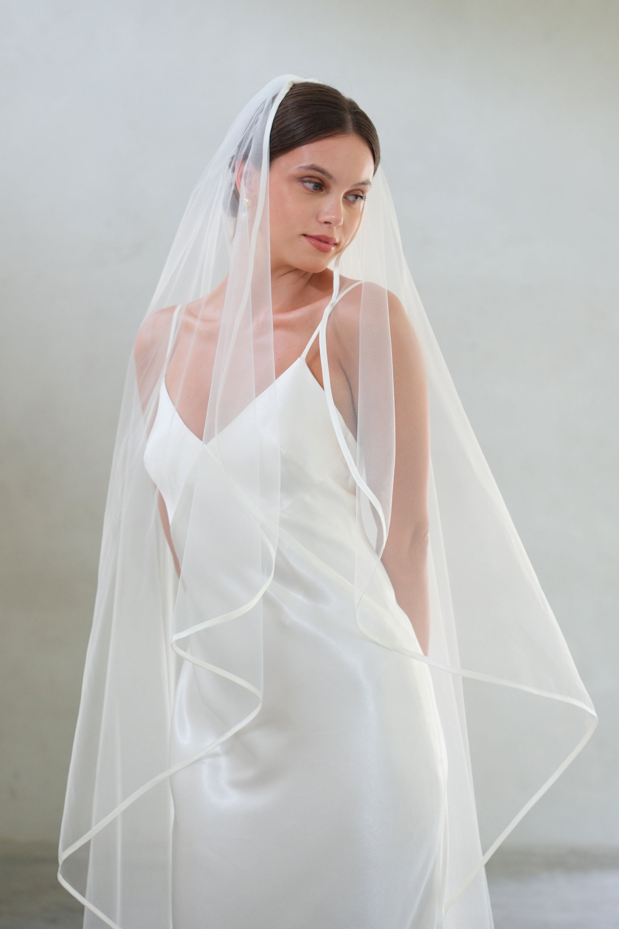 Half length front facing bride wears one-tier veil with fine satin trim
