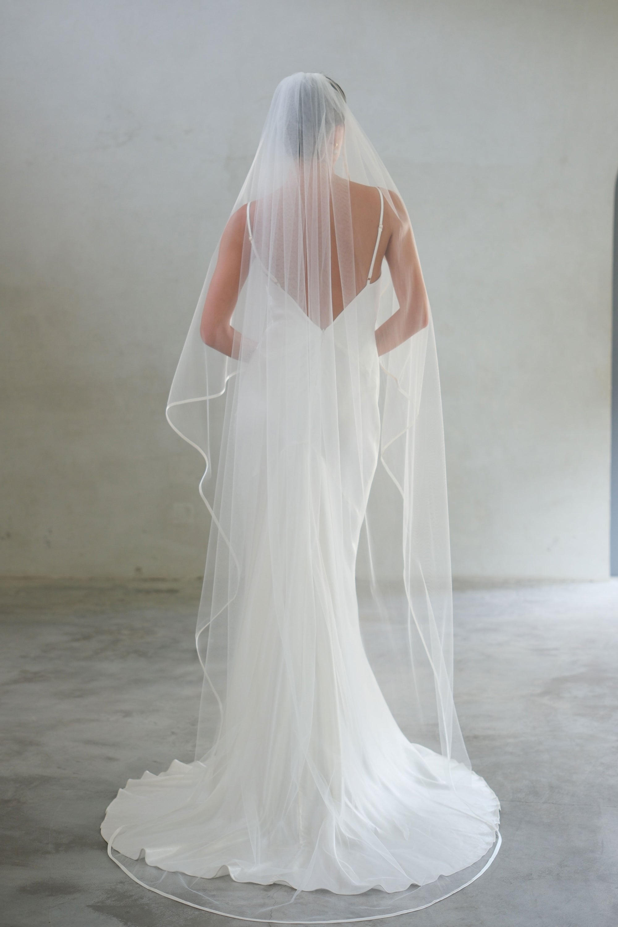 Full length back view of long wedding veil trimmed with satin ribbon and gathered at the comb