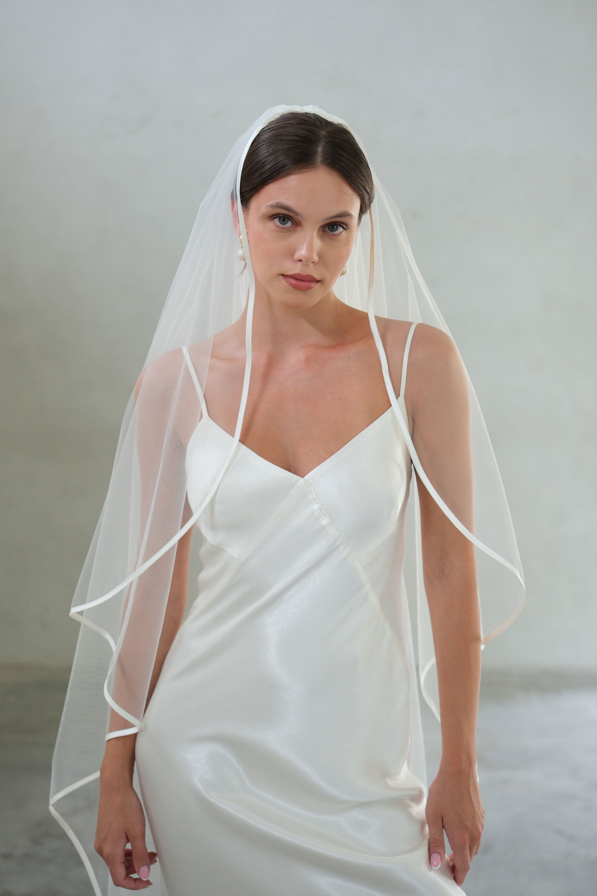 Half length front facing bride wears one tier veil trimmed with satin ribbon