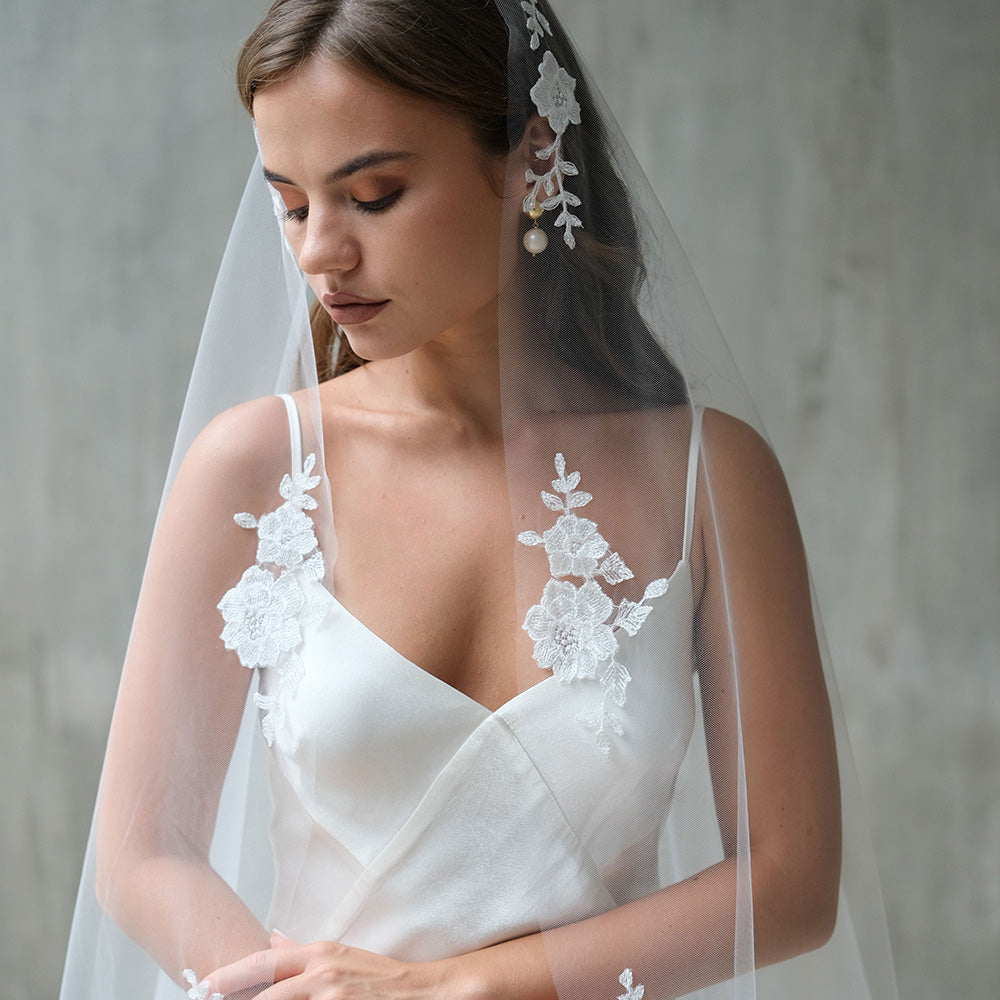 Floral embroidered mantilla veil falls over the hair annd shoulders of bride