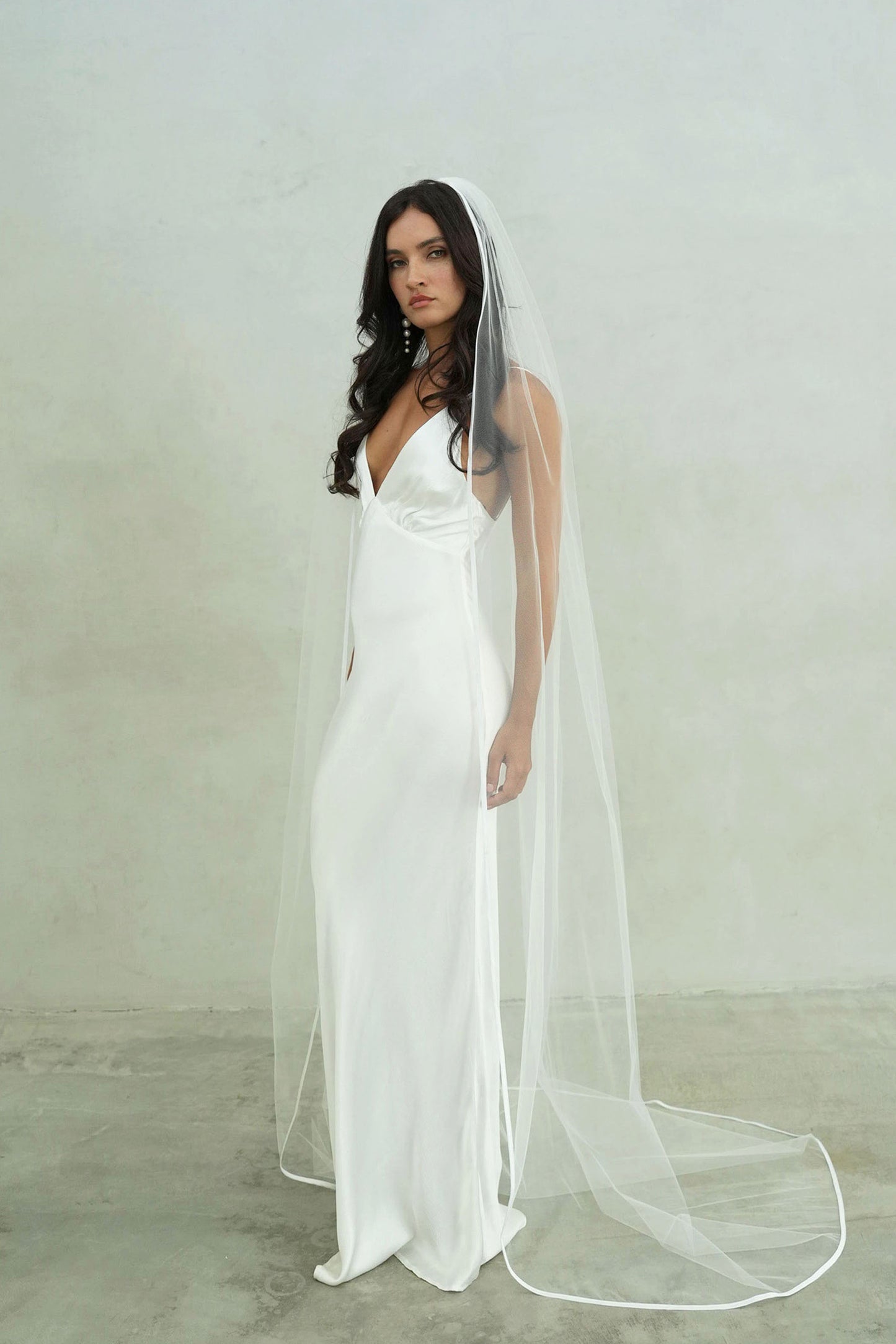 Full length bride wears long, one tier wedding veil trimmed with satin ribbon