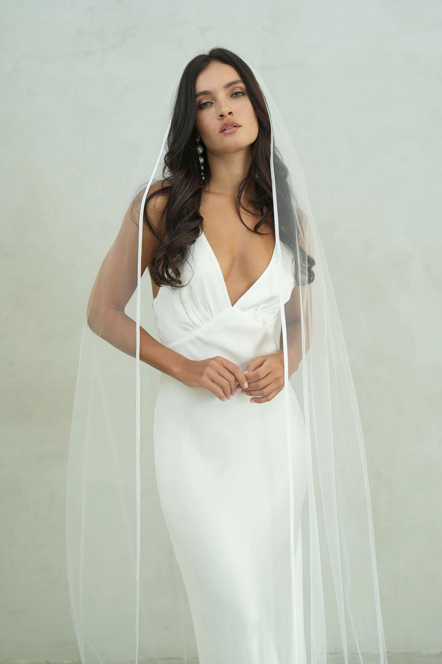 front facing bride wears long, one tier wedding veil trimmed with satin