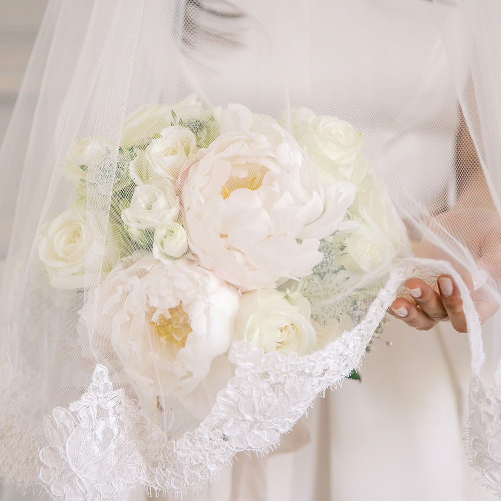 Close up of bridal bouquet and lace trimmed drop veil
