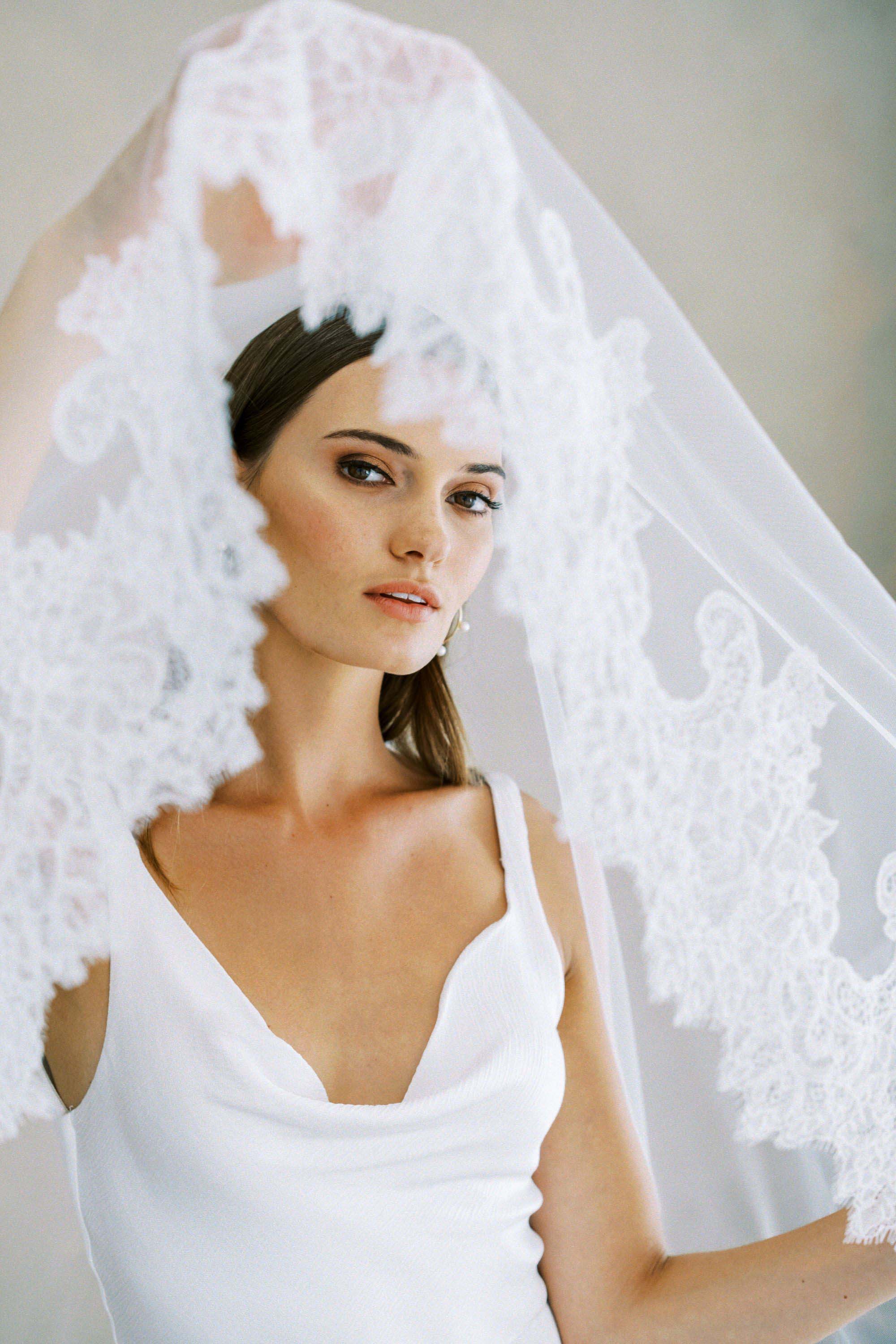 Model wears a mantilla lace wedding veil, drop veil with lace trim.