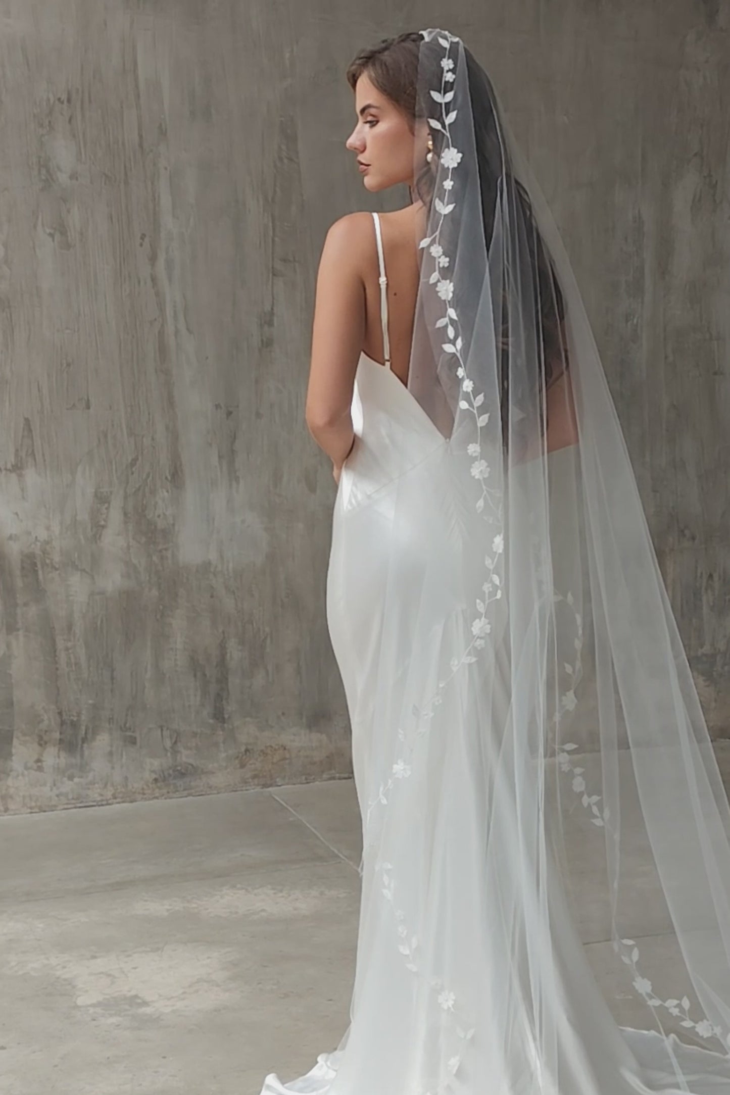 Back view of bride in profile shows long, mantilla style wedding veil edged with floral embroidery