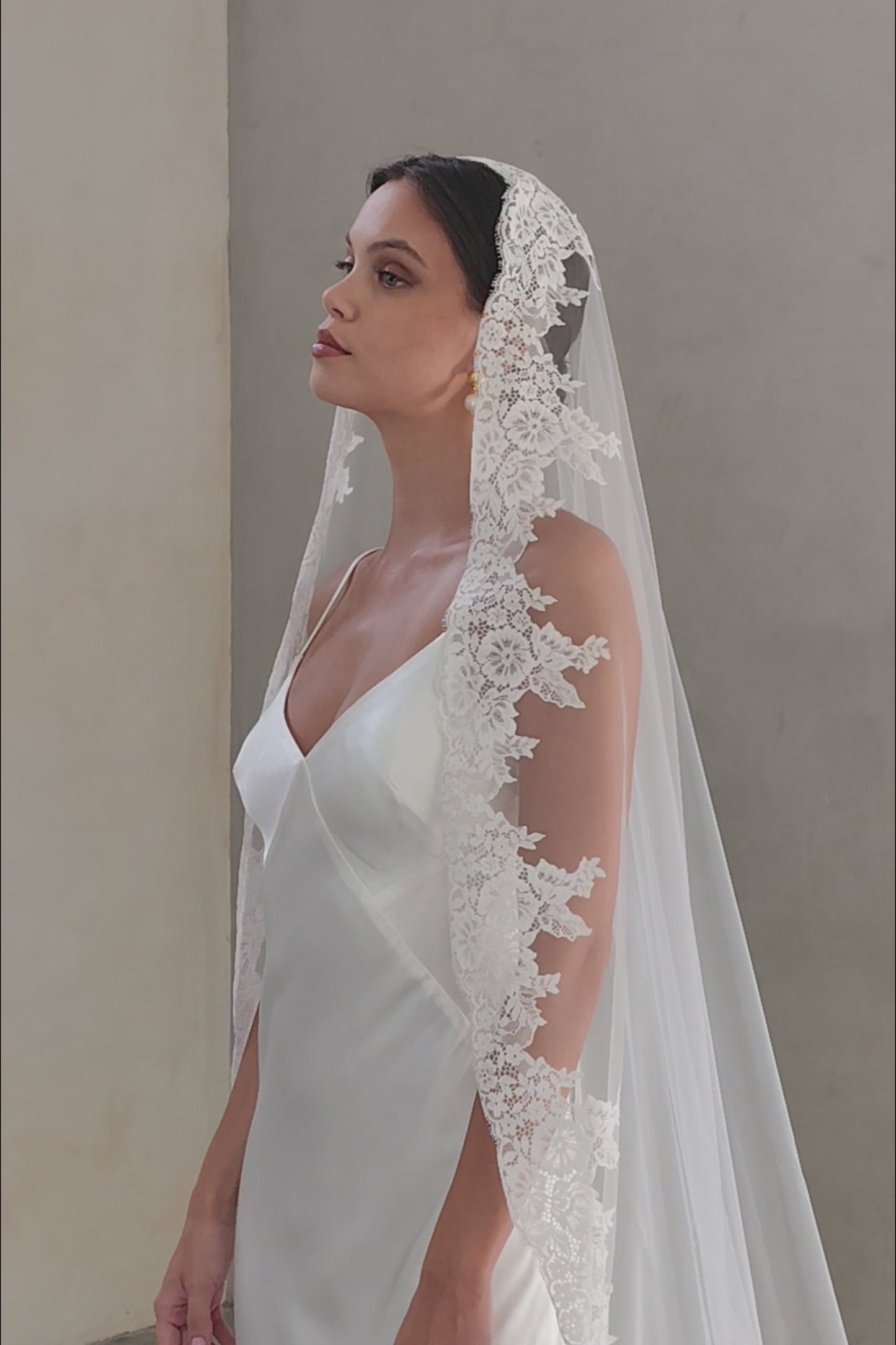 Half length shot of bride in profile wearing long, one-tier wedding veil with lace edging