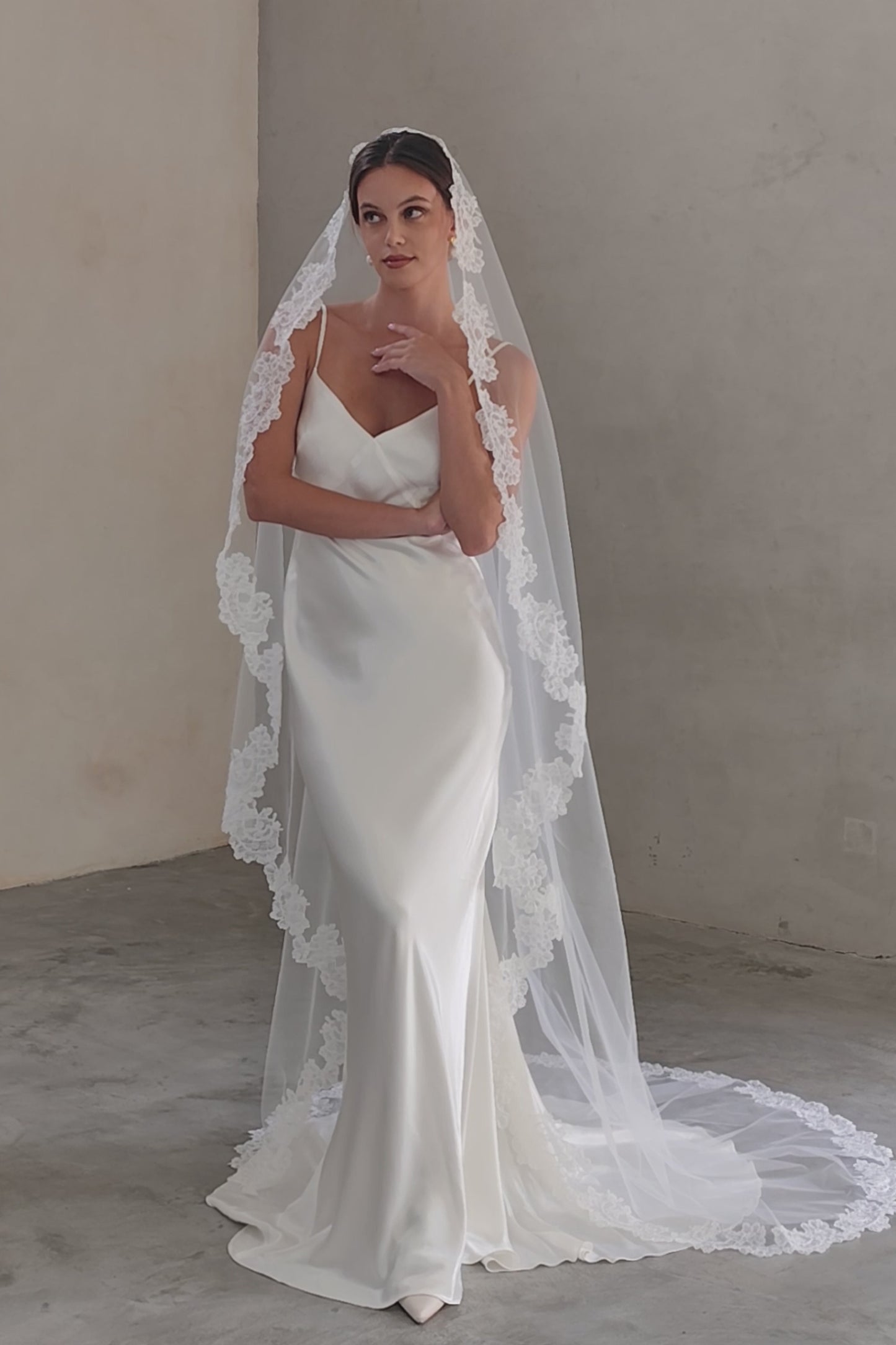 Full length front facing bride wearing long mantilla veil trimmed with floral lace