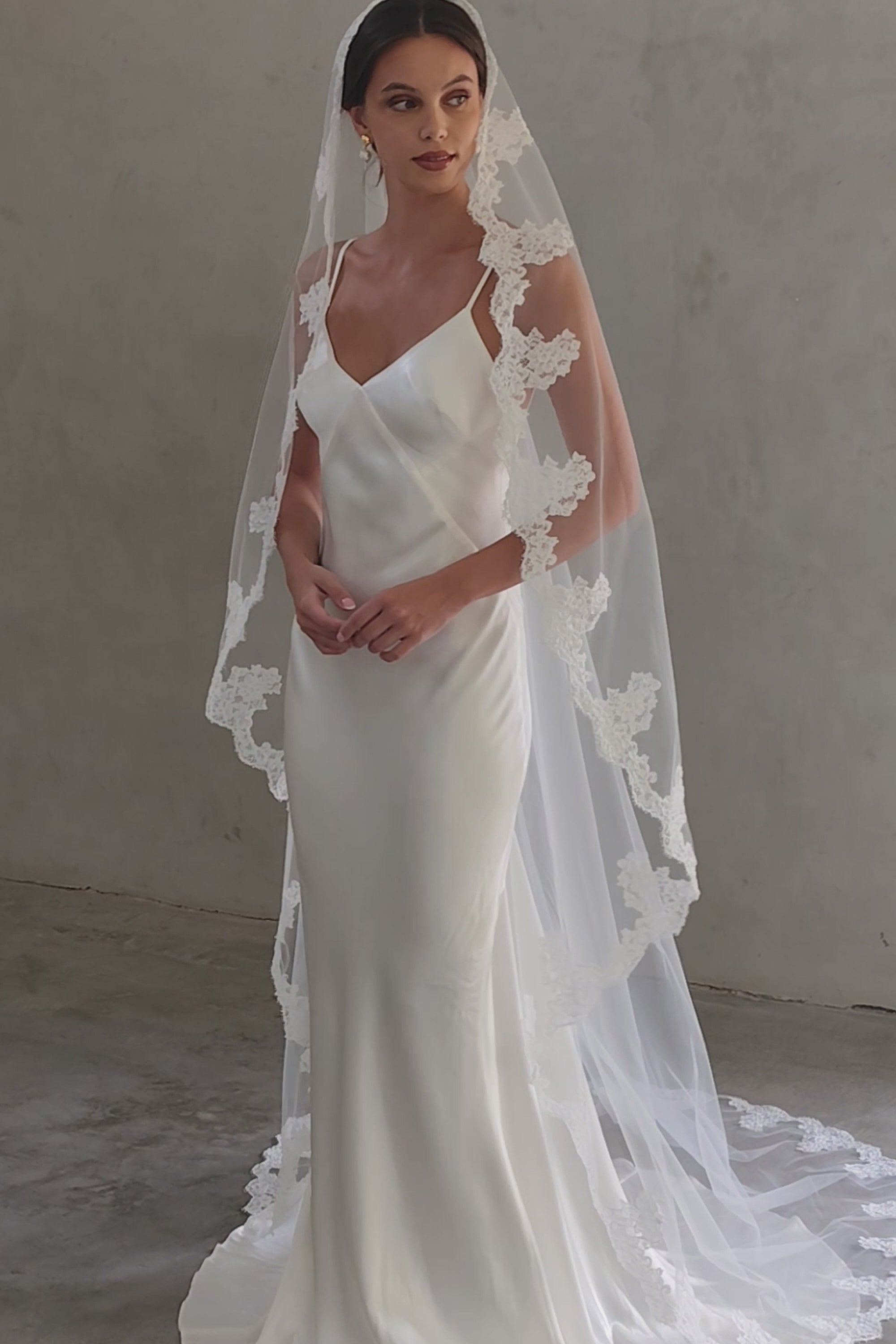 Full length front facing bride wears long, lace trimmed wedding veil