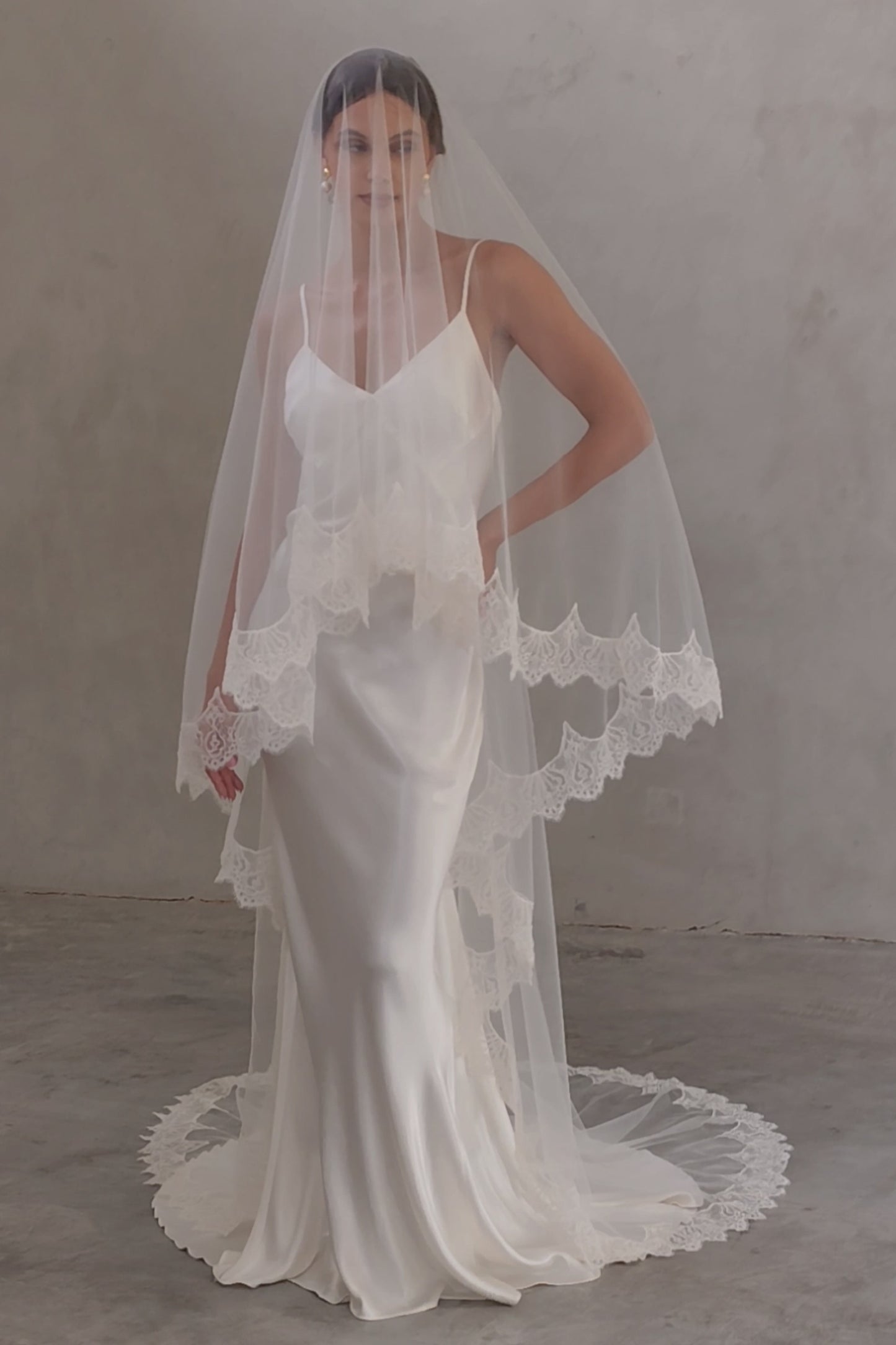 Full length front facing bride wears two tier, laced trimmed veil in chapel length; blusher down