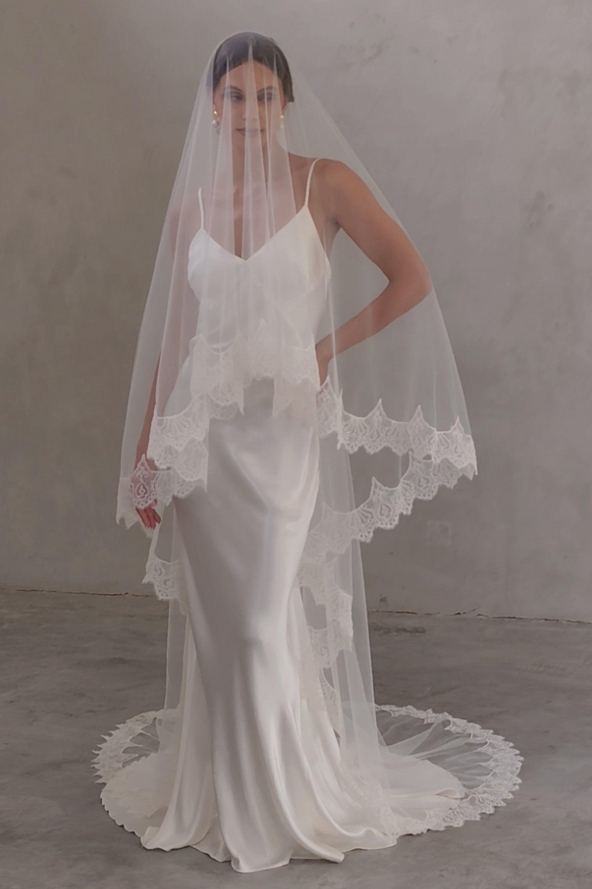 Full length front facing bride wears two tier, laced trimmed veil in chapel length; blusher down