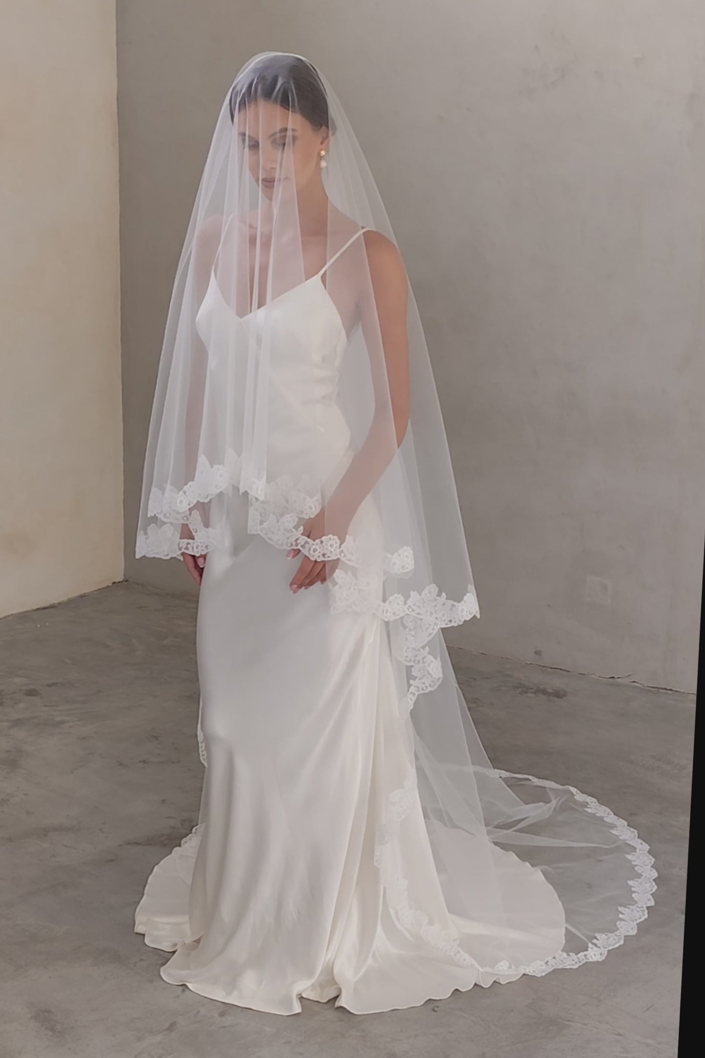Full length front view of bride wearing long, laced edged veil in chapel length - blusher is down