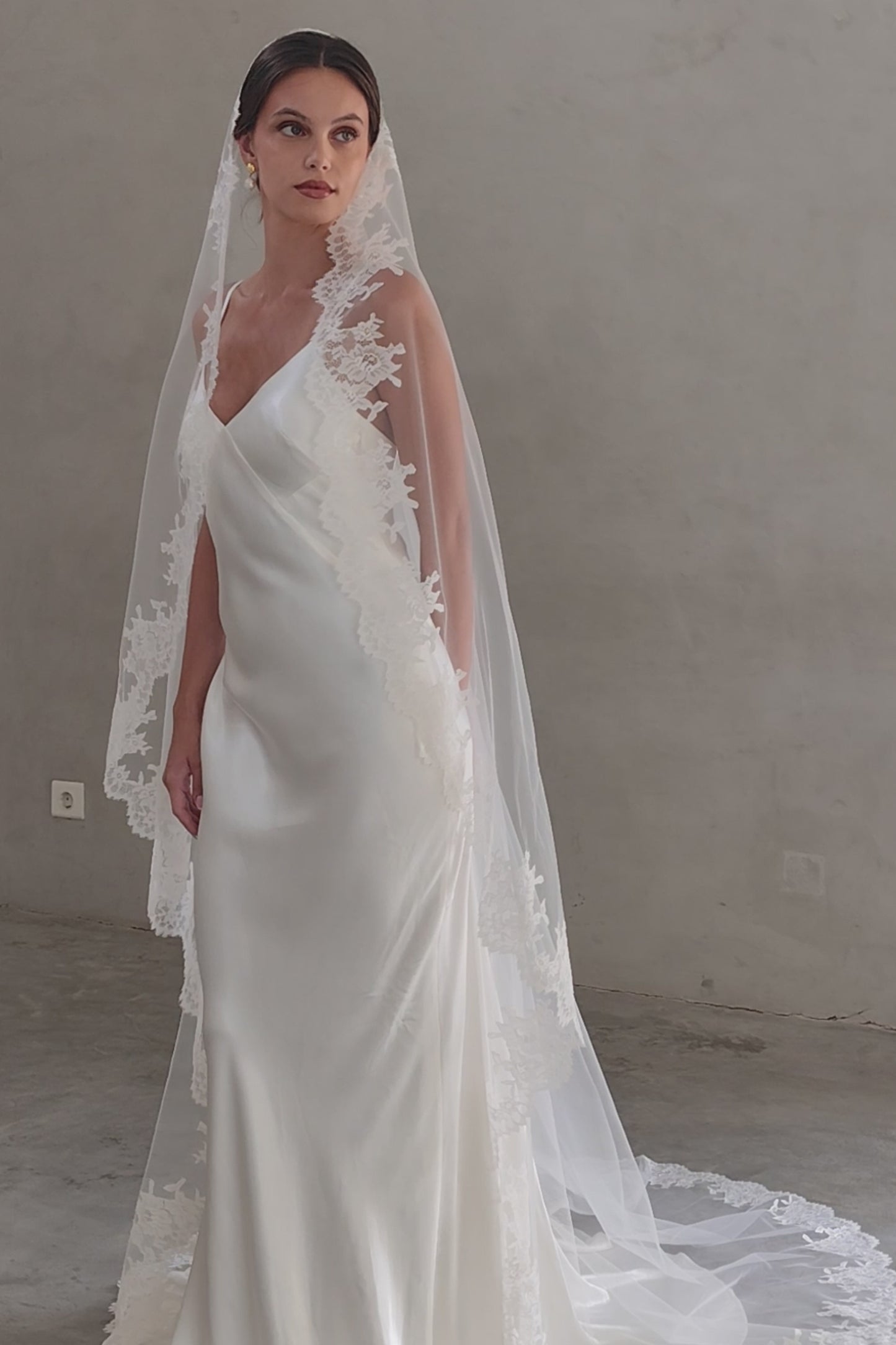 Full length front facing bride wears long mantilla wedding veil with floral lace trim