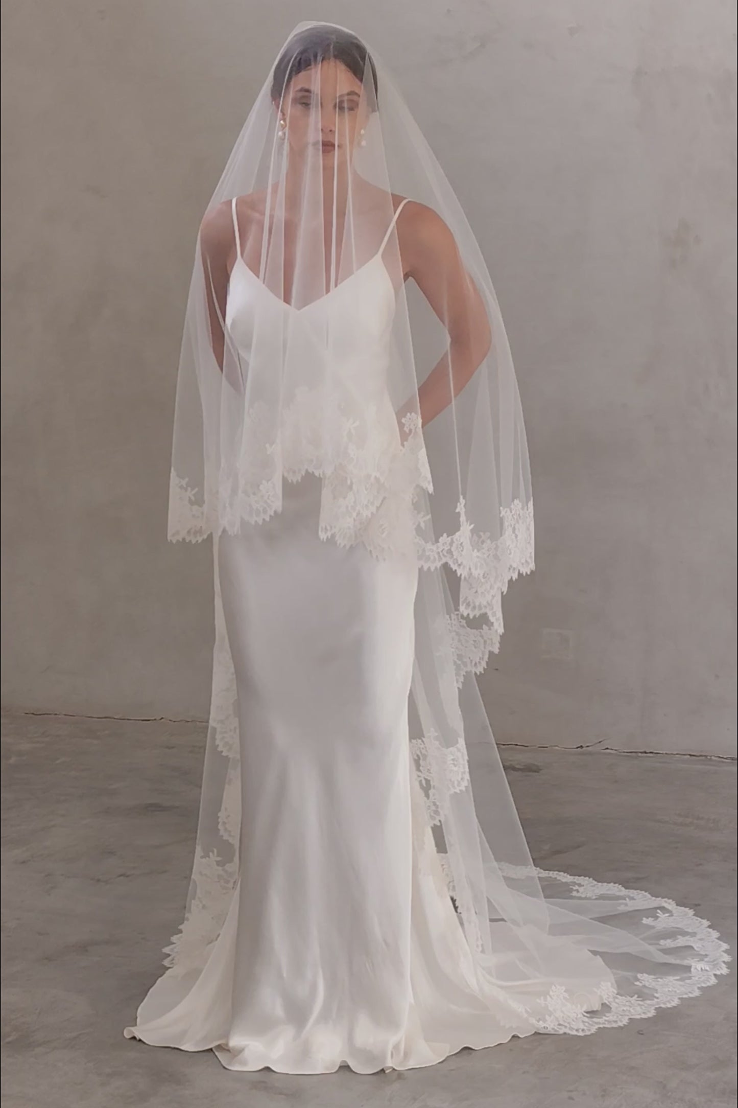 Full length front facing bride wears long, two tier veil with lace edge and blusher over the face