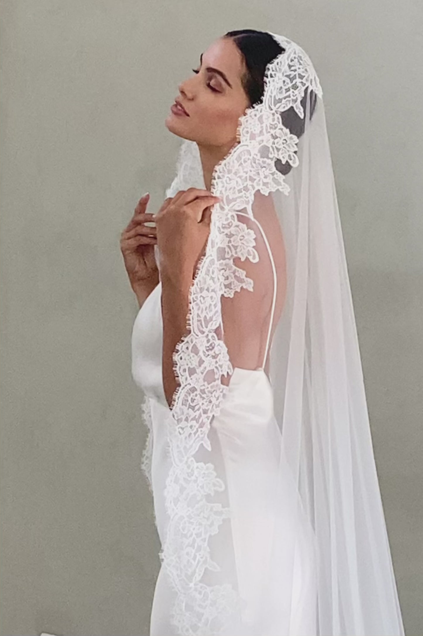Half length side view of bride wearing long, lace edged mantilla veil