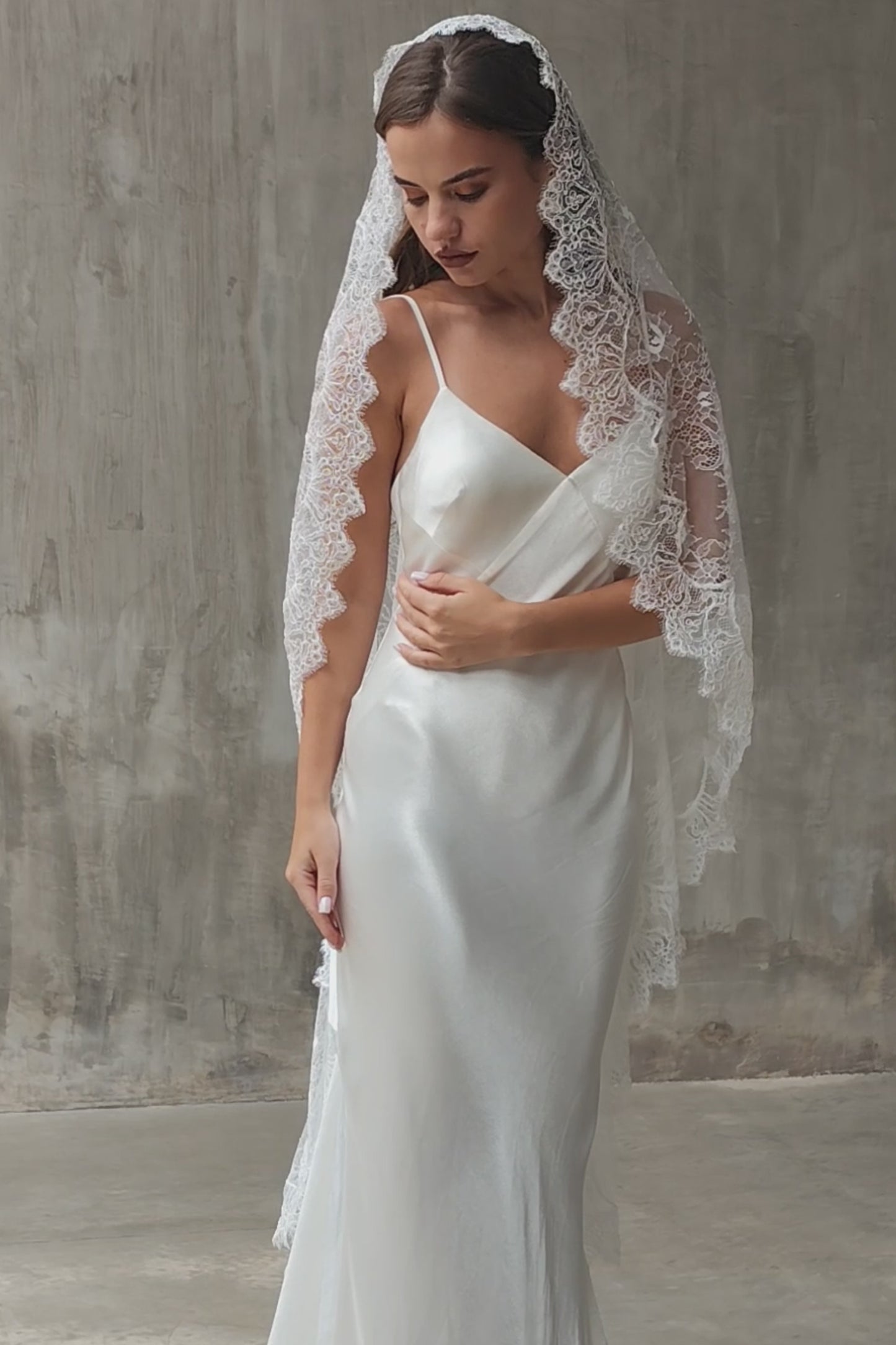 Full lace mantilla wedding veil drapes over the hair and shoulders of front facing bride