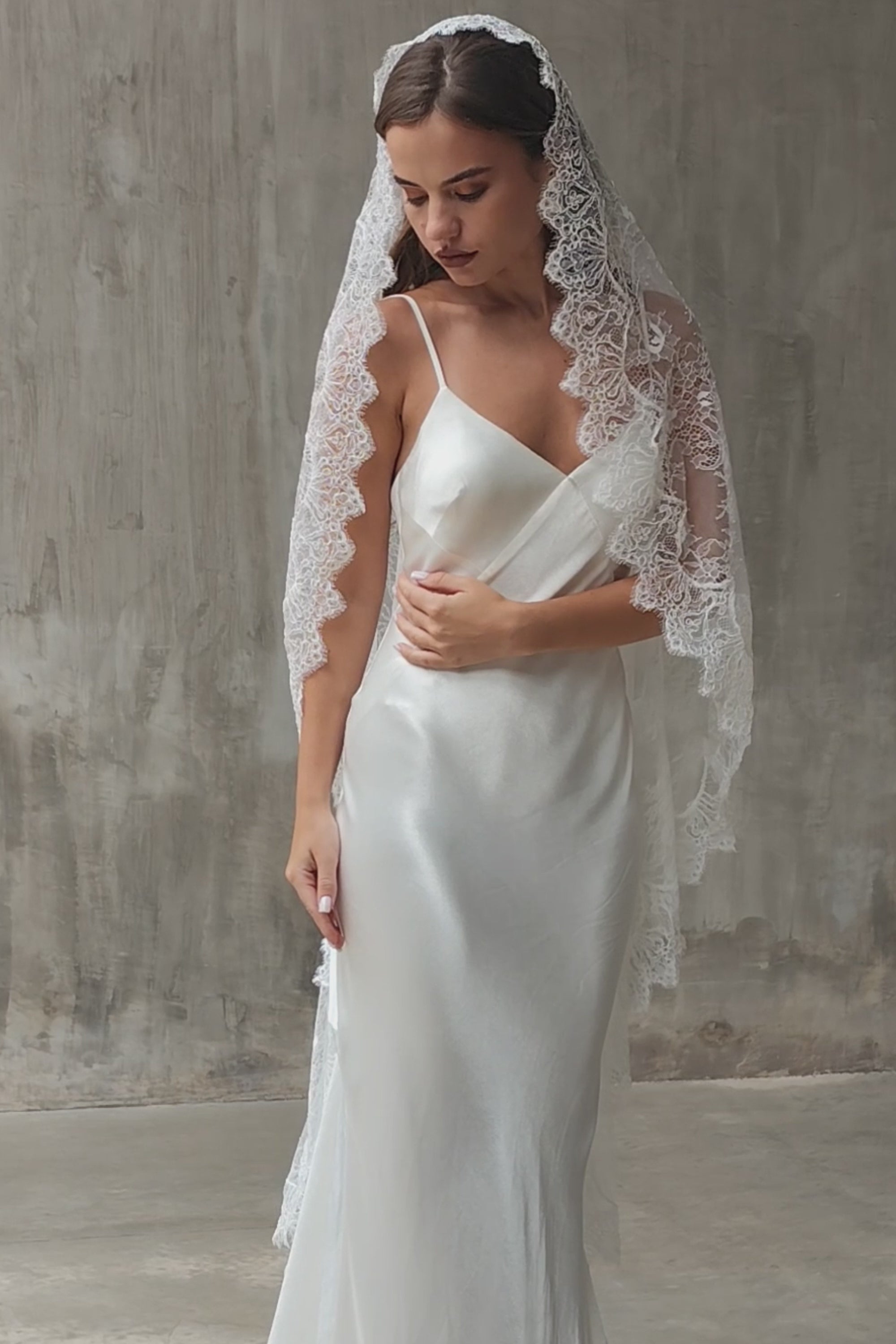 Full lace mantilla wedding veil drapes over the hair and shoulders of front facing bride