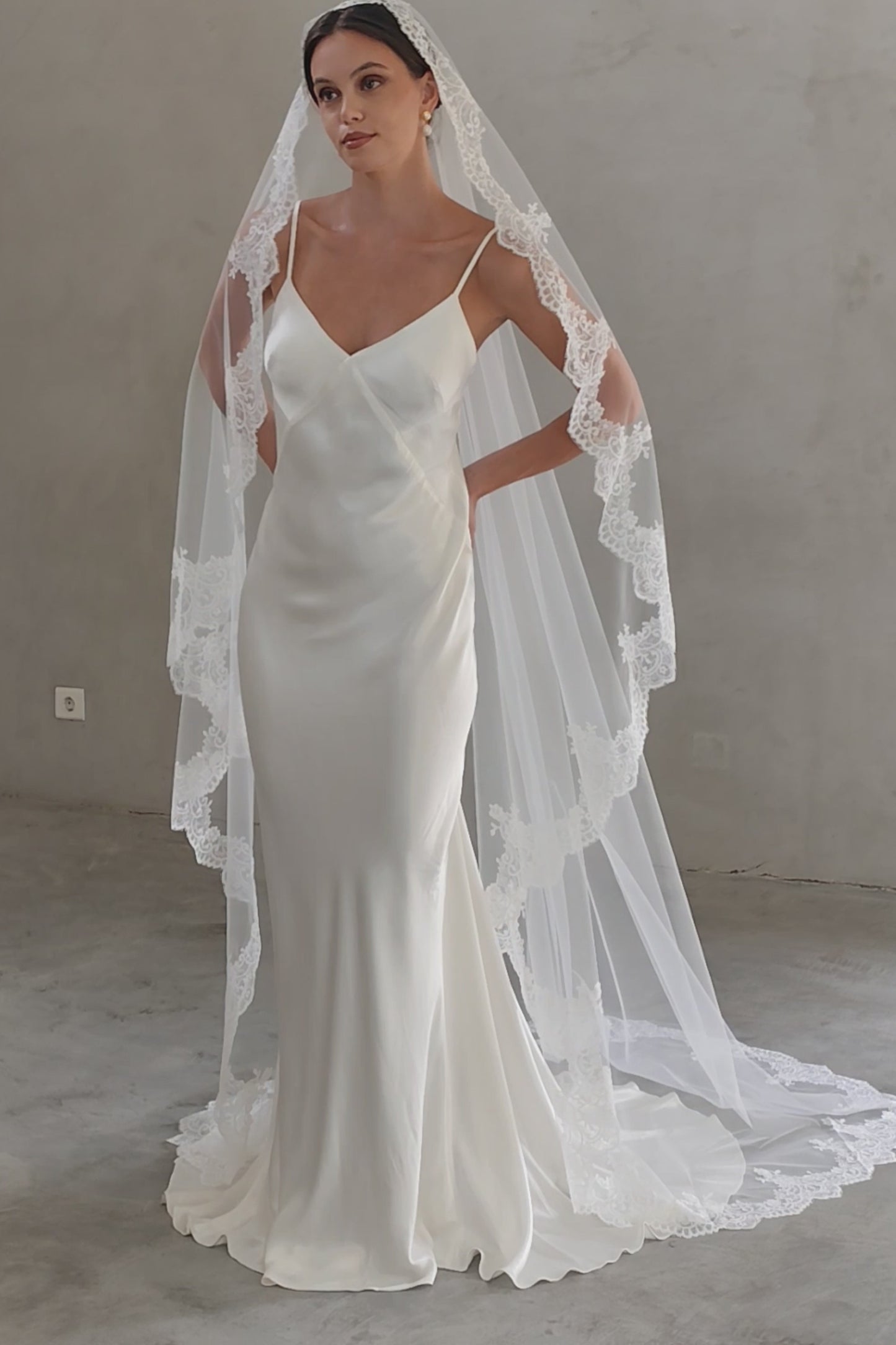 Full length front facing bride wears romantic mantilla style long veil with lace trim