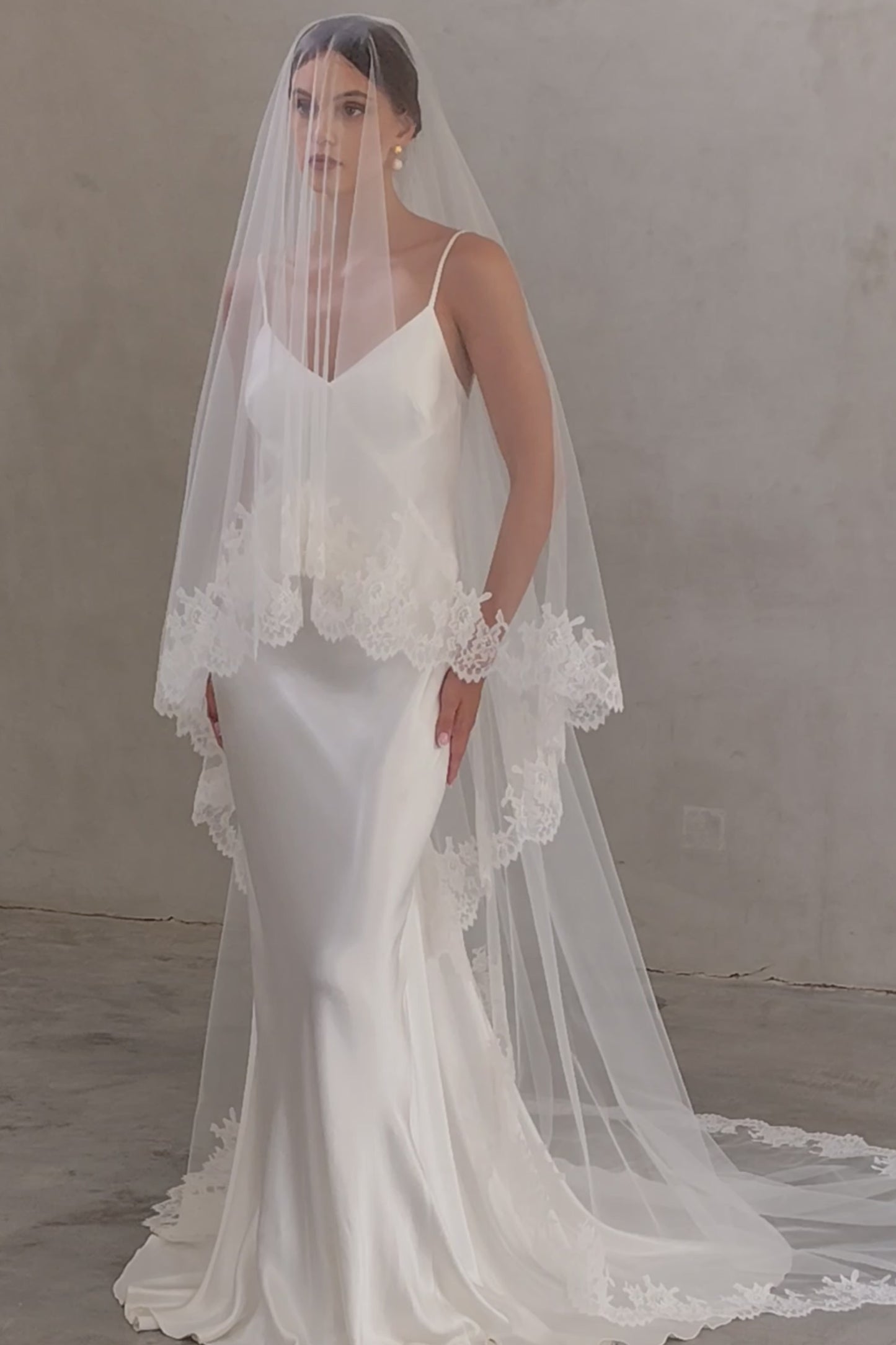 Full length front facing bride wears blusher down on chapel length wedding veil featuring lace trim