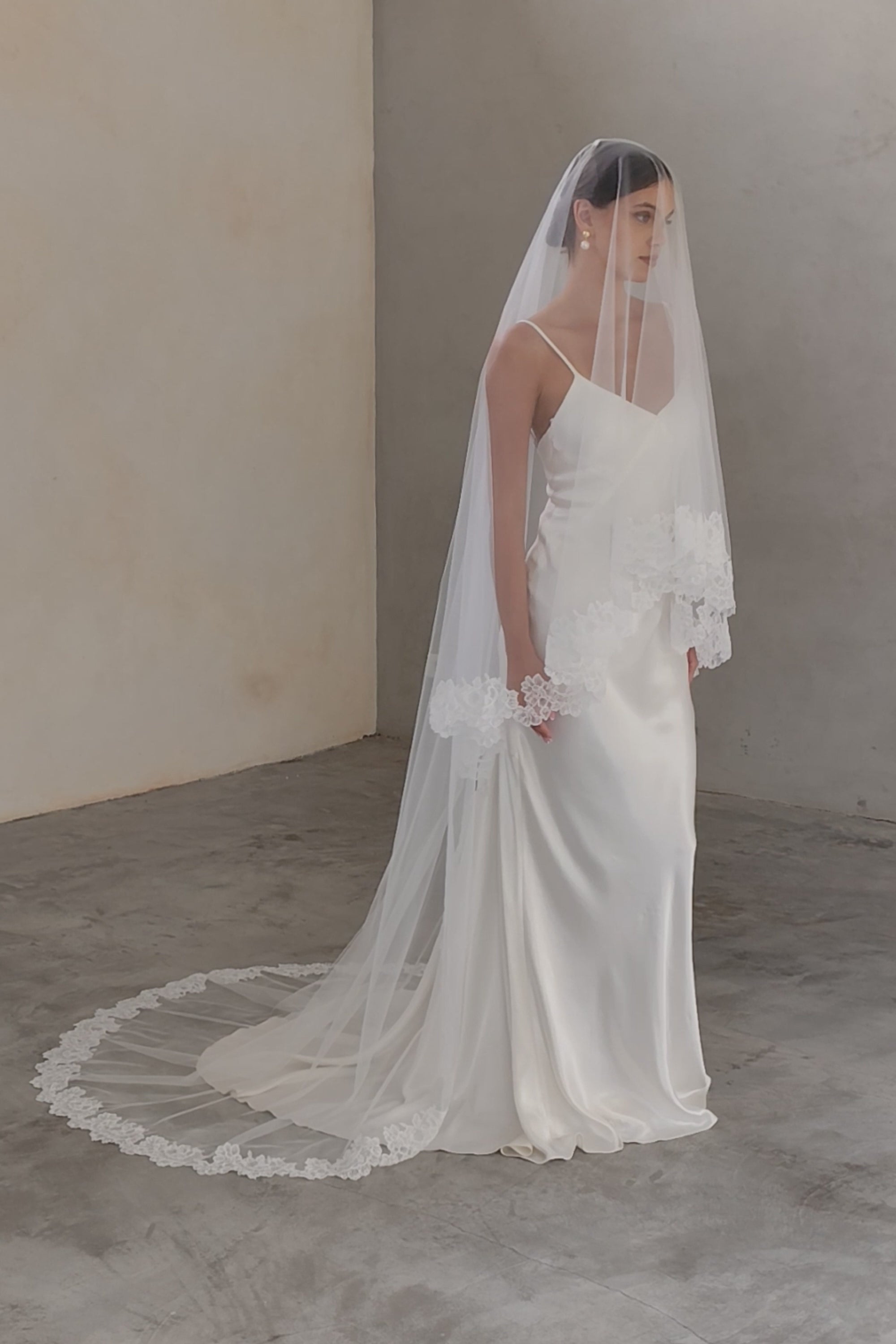 Full length view of bride wearing lace trimmed wedding veil in chapel length; blusher down