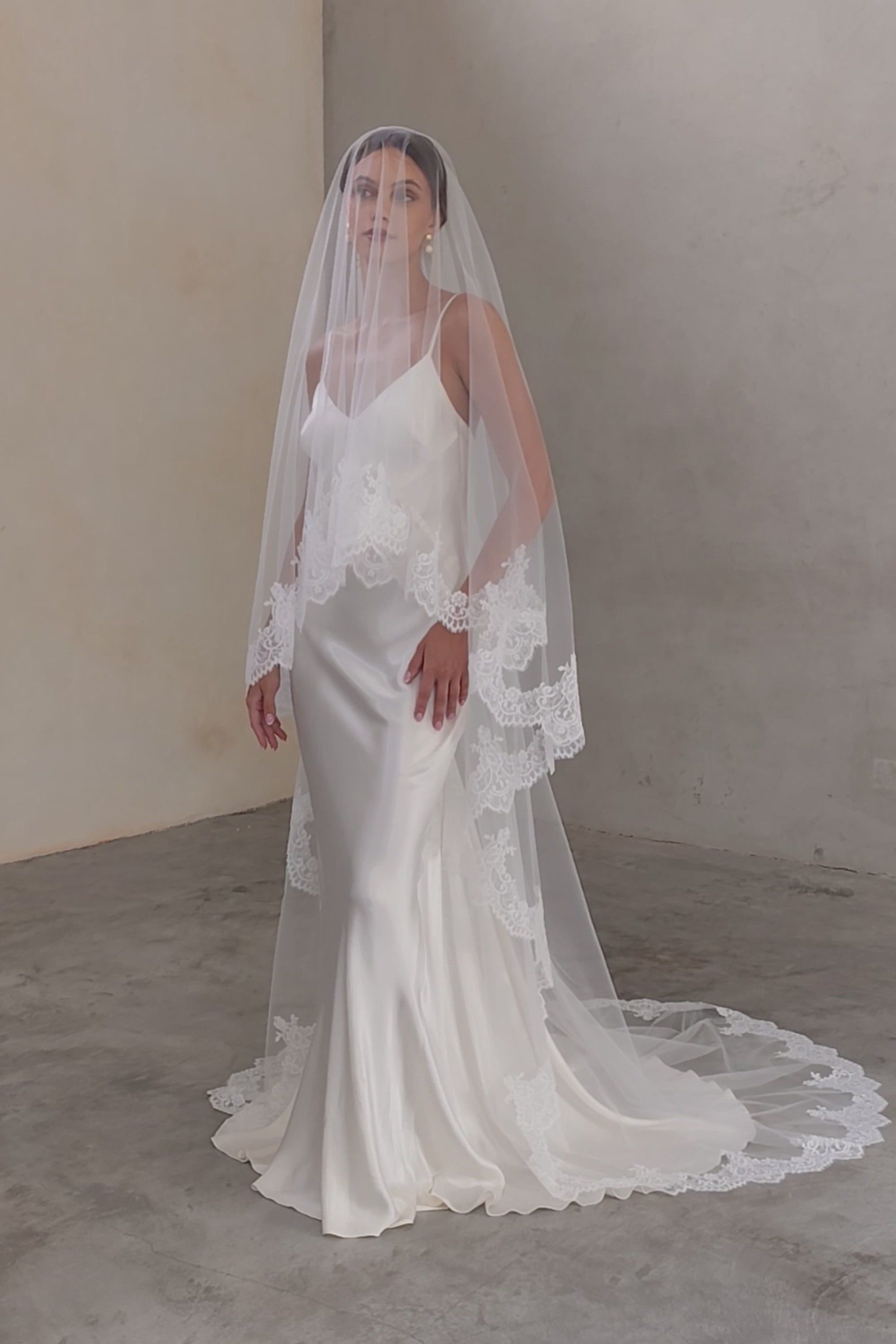 Full length front-facing bride wears long, lace-edged drop-veil; blusher down