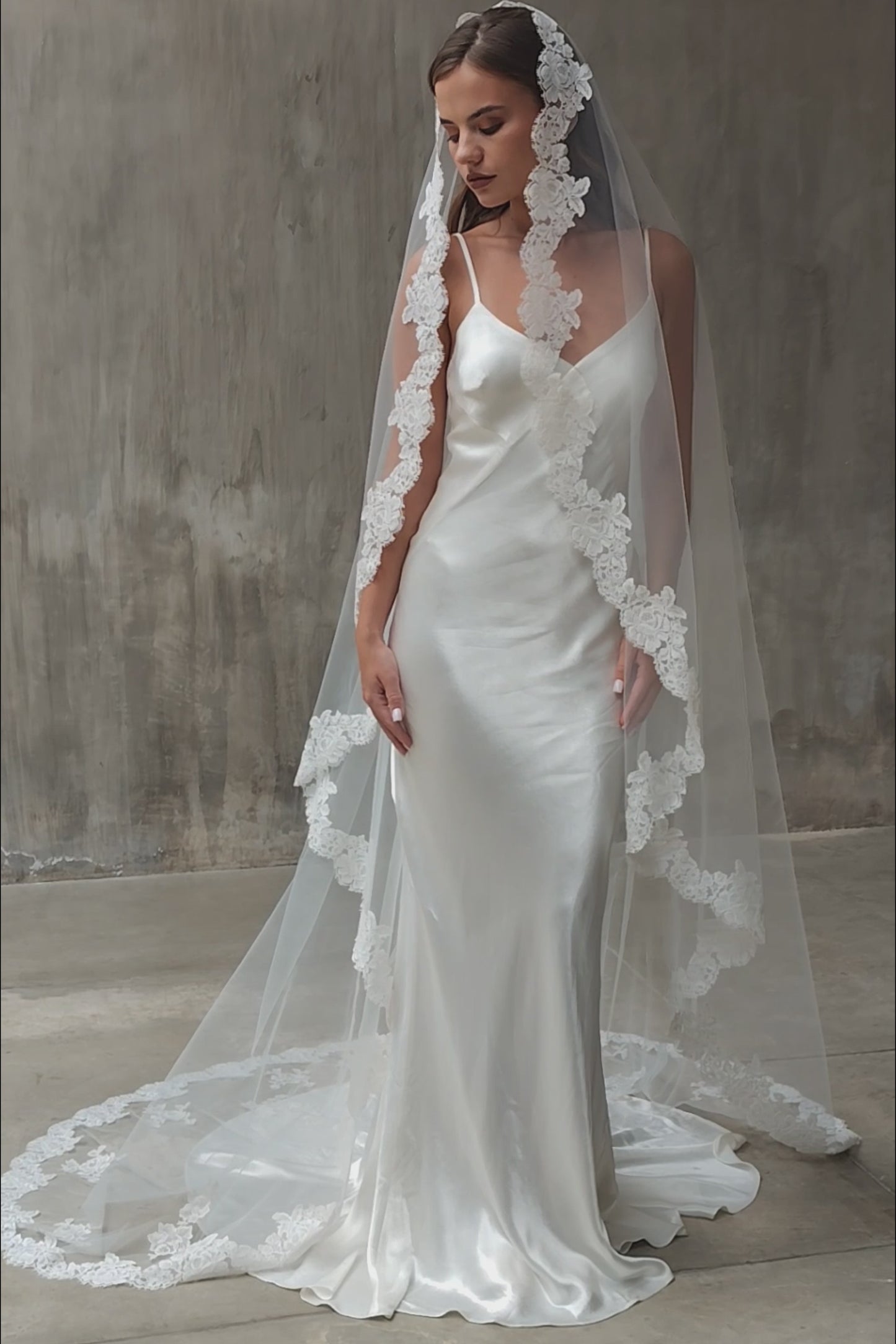 Full-length front side view of a bride wearing long one-tier mantilla lace edged veil