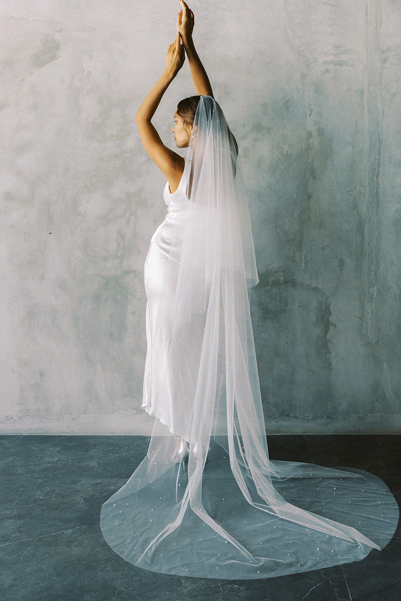 A model wearing a two tier wedding veil with pearls in chapel length