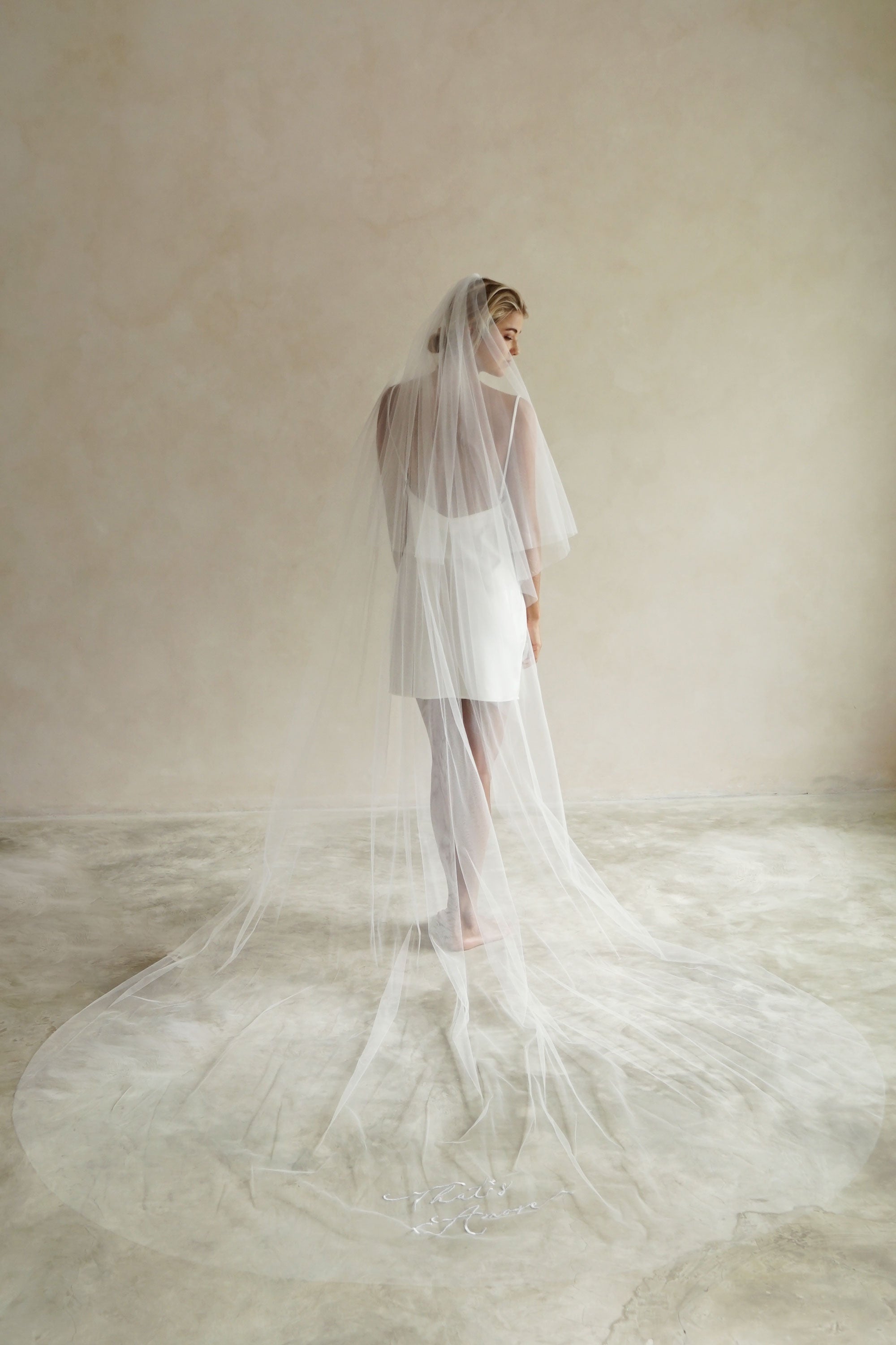 A model wearing a long wedding veil with embroidery text that&#39;s amore