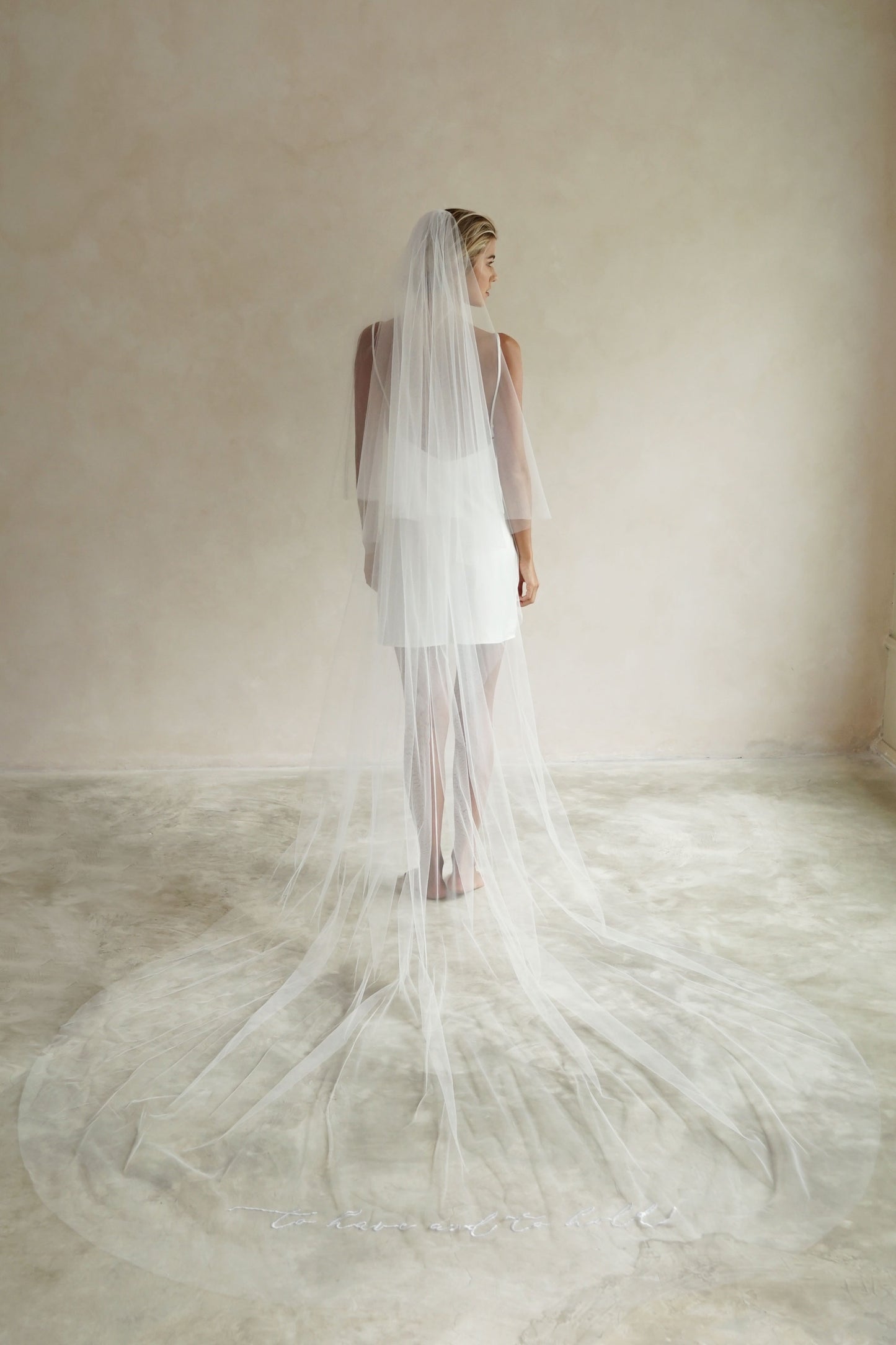 A model wearing a wedding veil with embroidery text to have and to hold