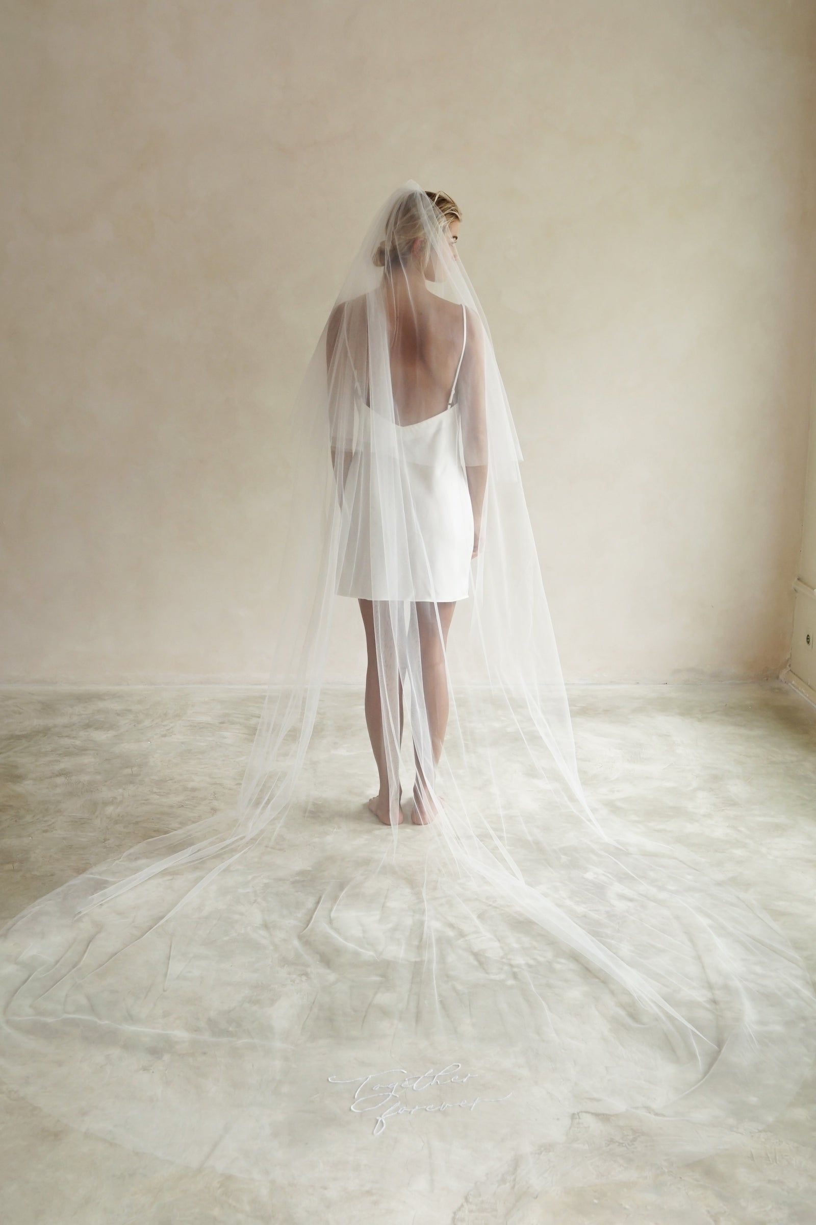 A model wearing a long wedding veil with embroidery text together forever