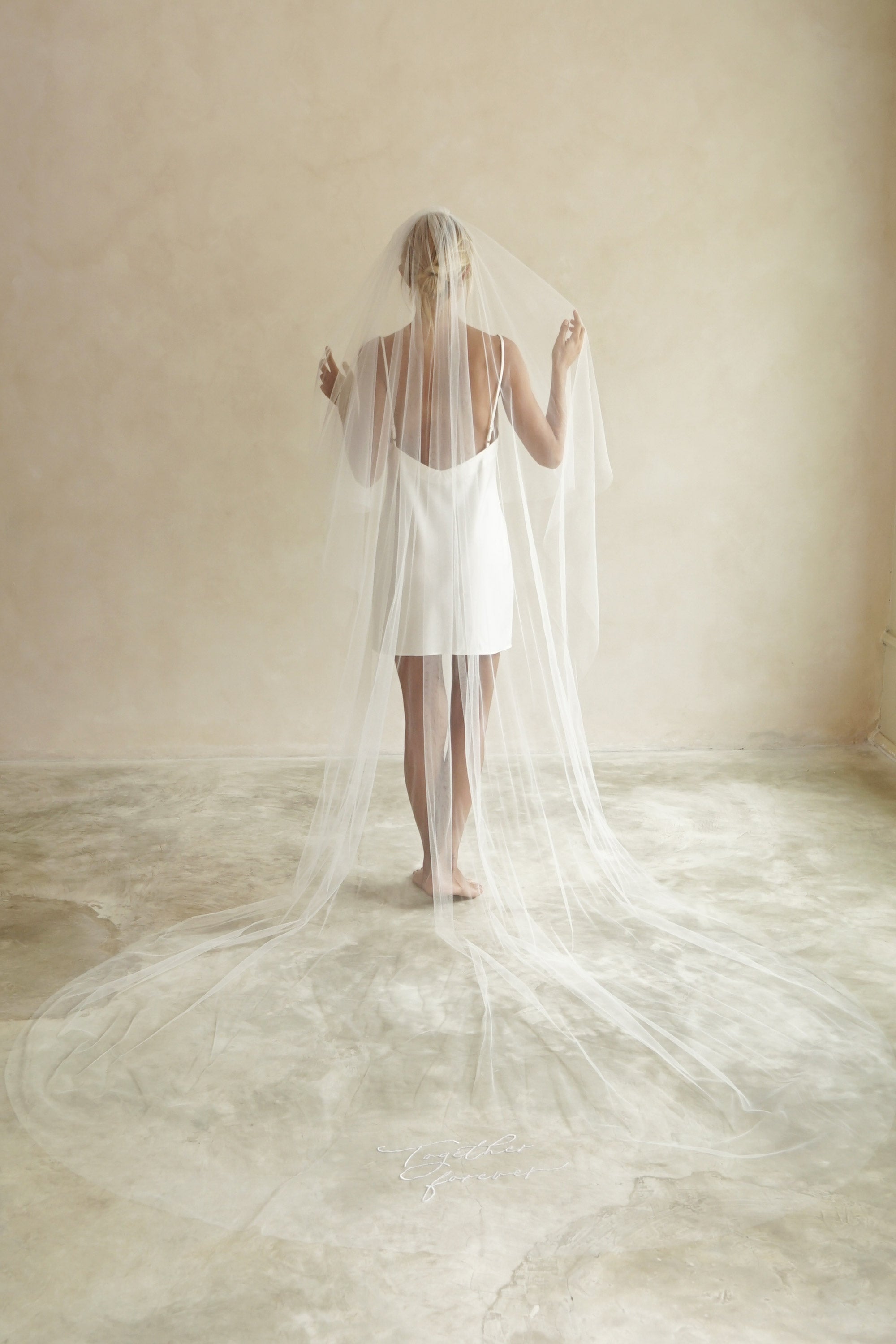 A model wearing a long wedding veil with embroidery text together forever