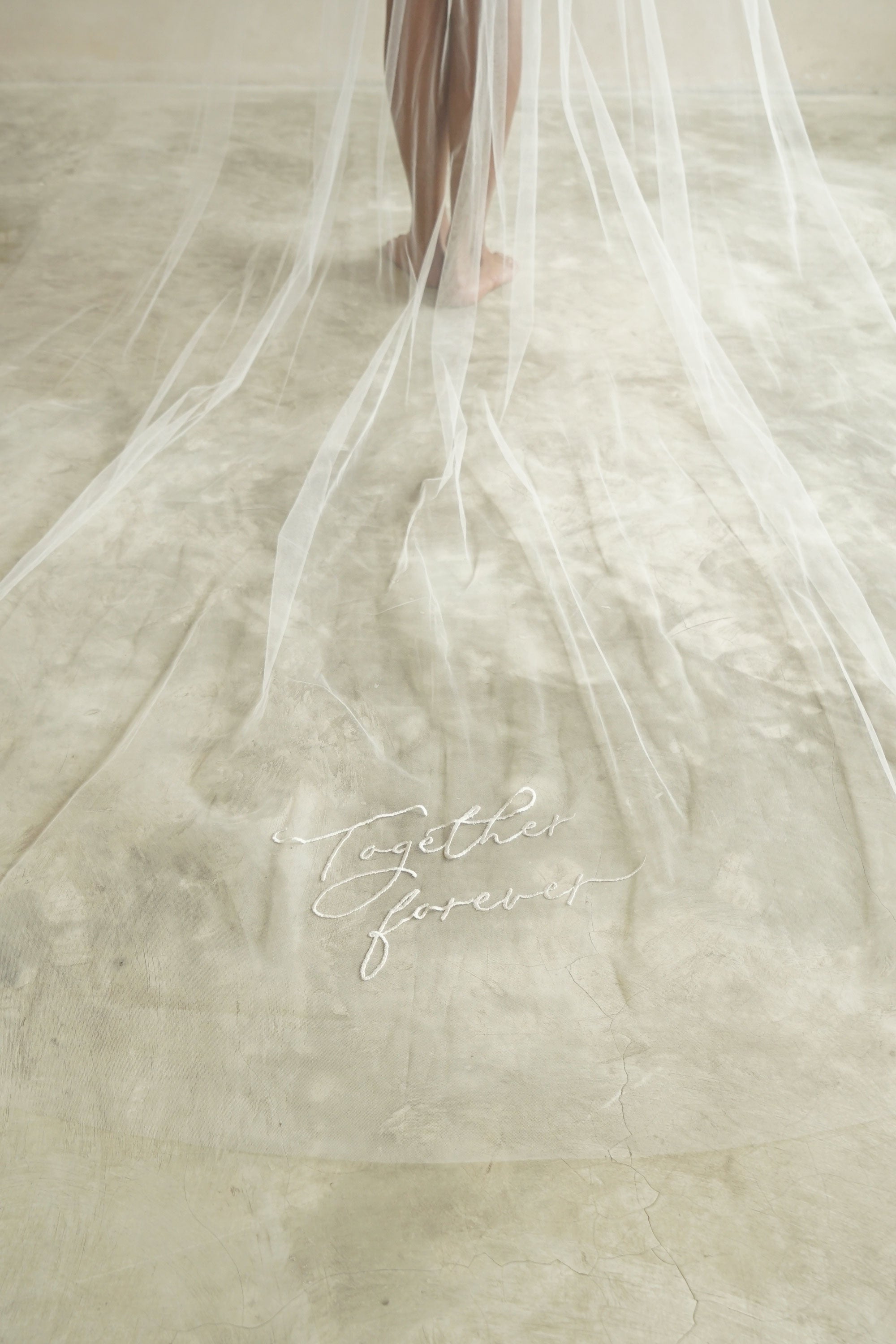 A model wearing a long wedding veil with embroidery text together forever