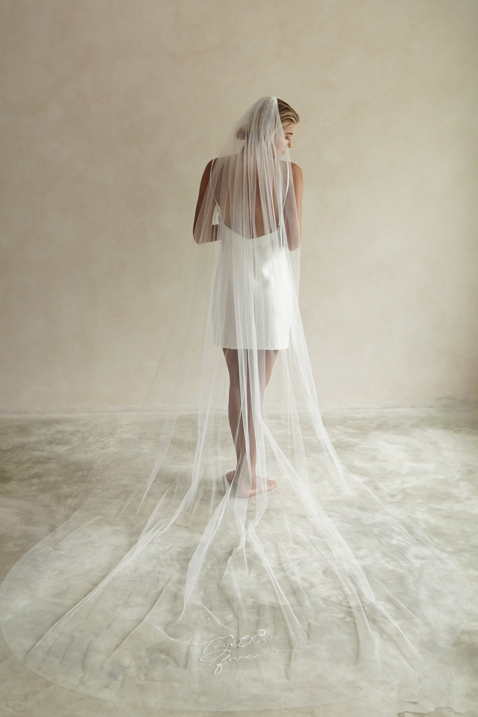 A model wearing a long wedding veil with embroidery text together forever